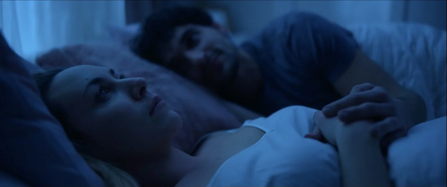 An image of a woman lying awake in bed, beside her partner.