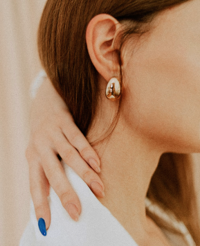 Close-up of a woman with a gold hoop earring, touching her neck with her hand, wearing a white shirt.