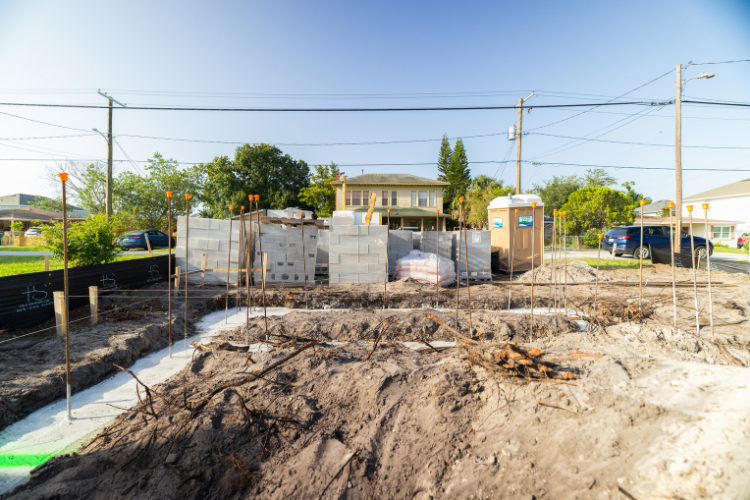 Construction site with dirt, cinder blocks, and portable toilet in a residential neighborhood.