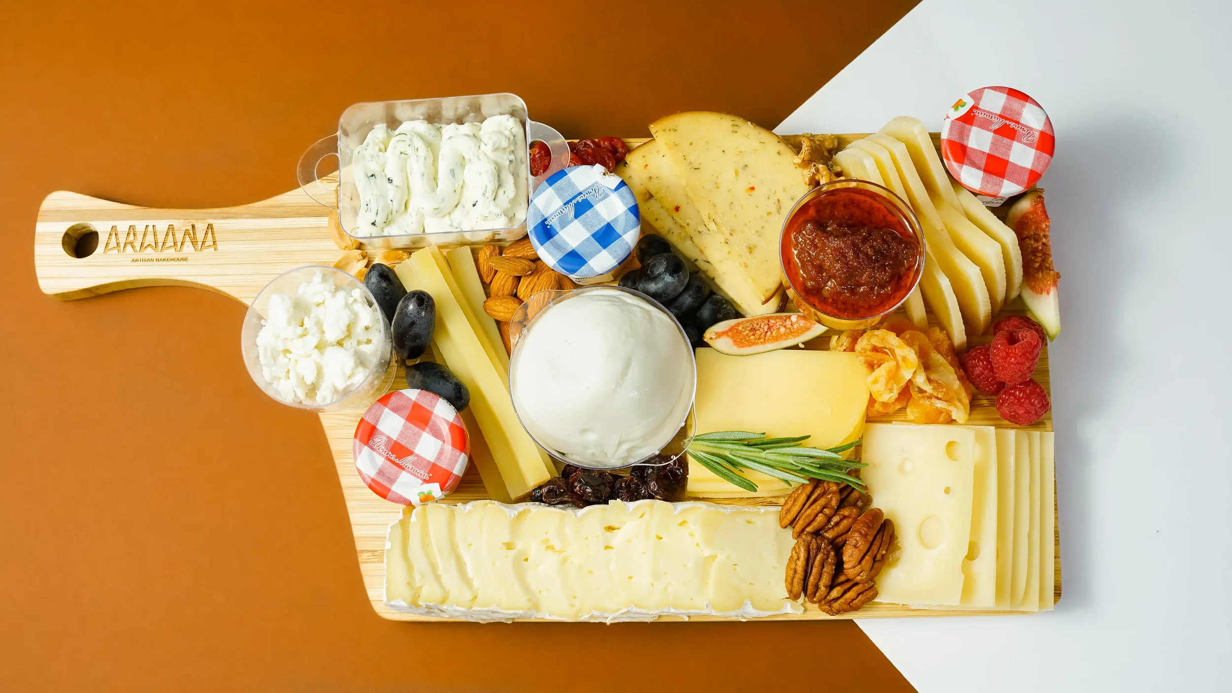 Artisan Bakehouse cheese and charcuterie platter with assorted cheeses, nuts, fruits and spreads on a branded wooden board, Riyadh