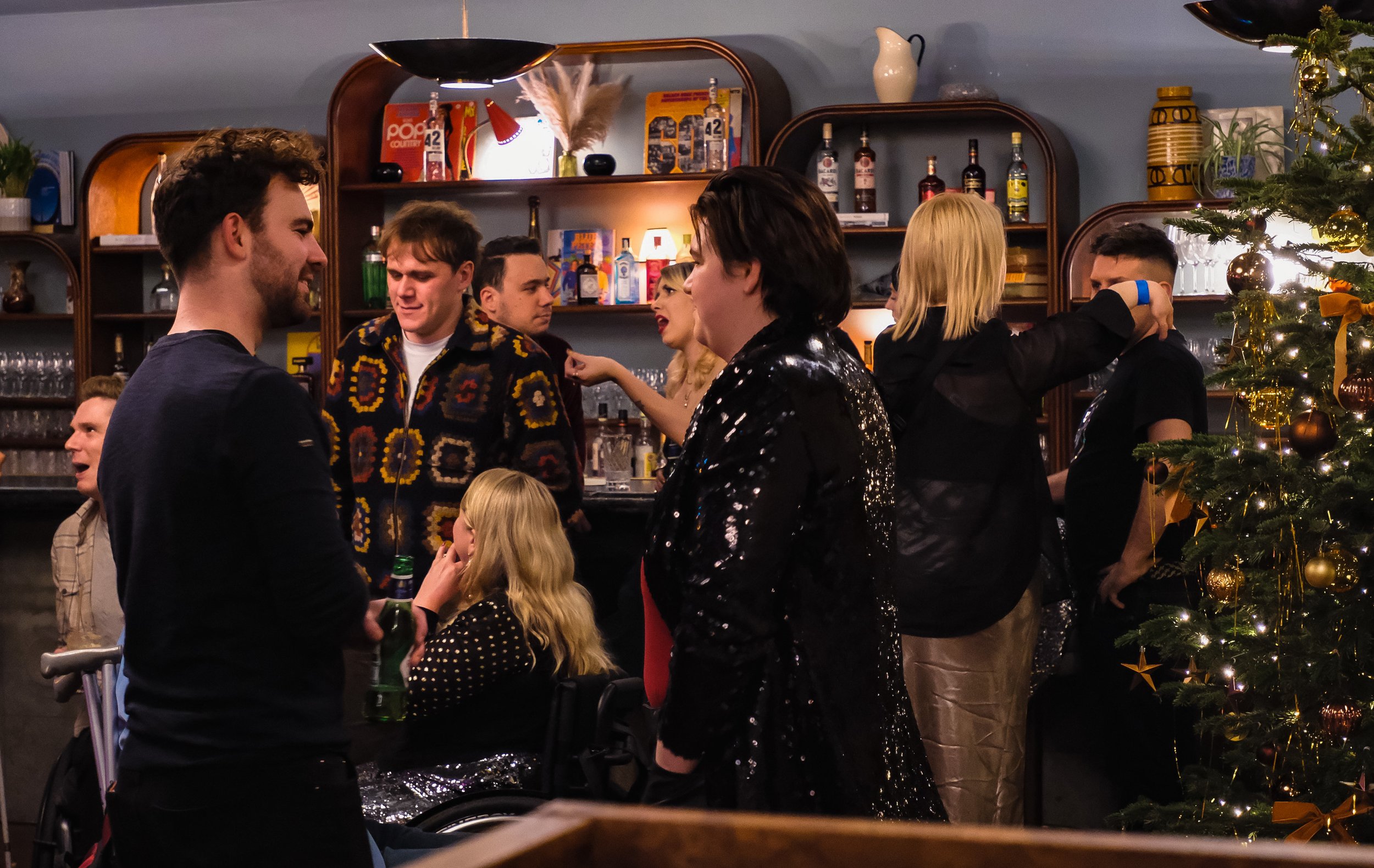 People socializing in a decorated bar beside a lit Christmas tree