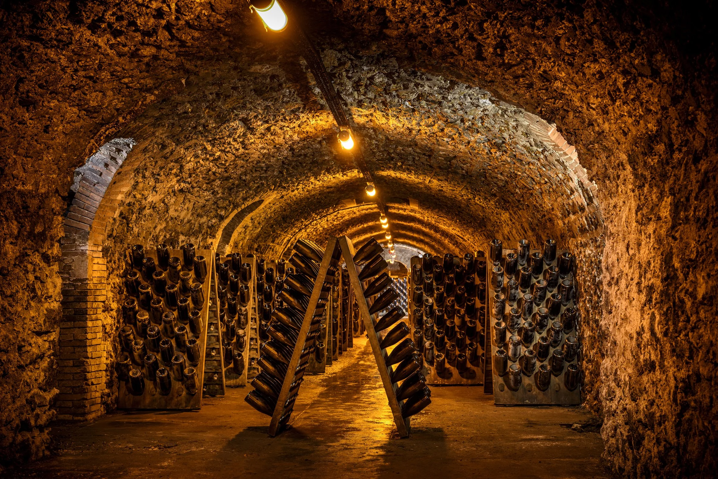 A wine cellar in Billecart-Salmon, Champagne, with an arched brick ceiling, dim lighting, and wine bottles stored on racks.