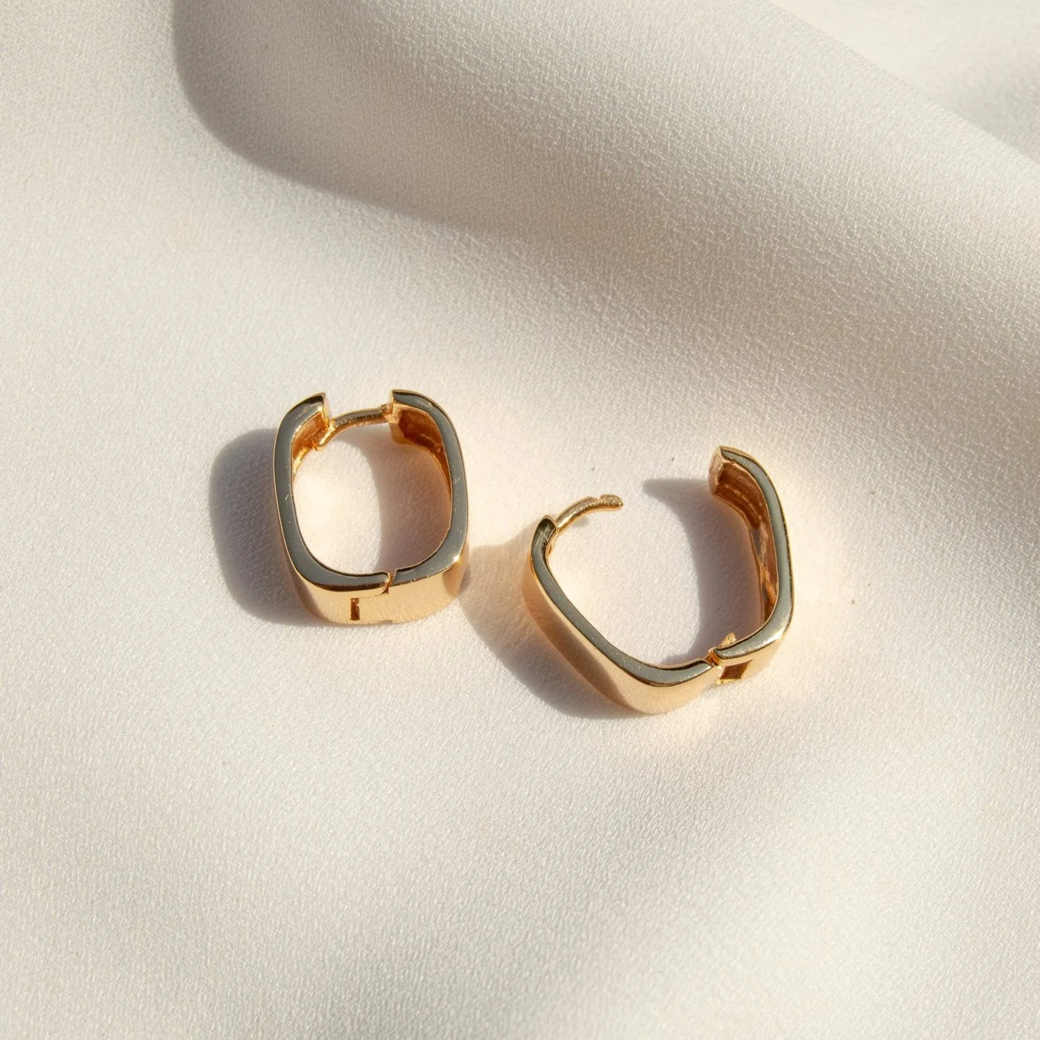 Gold and silver hoop earrings on a cream fabric surface