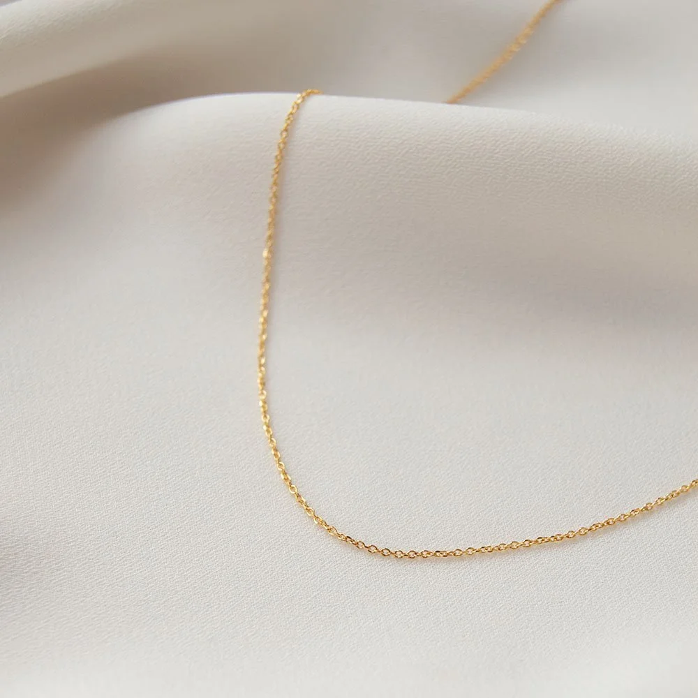 Close-up of a delicate gold chain necklace resting on white fabric.