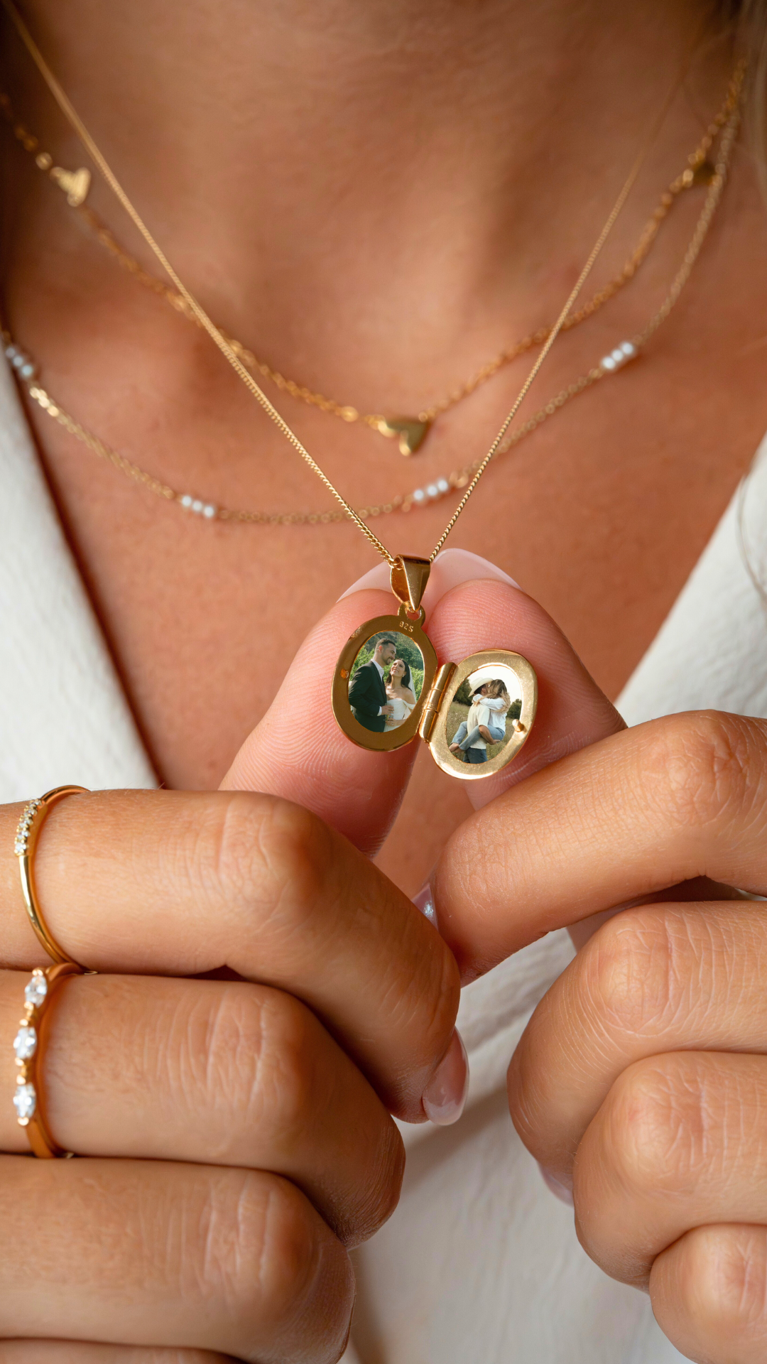 Close-up of a woman holding an open gold locket necklace with two photo images inside, showing a couple in wedding attire.