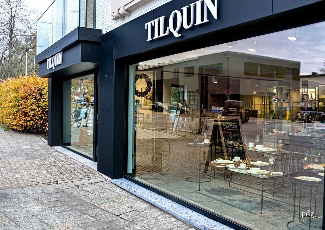 Front of a store with large glass windows and black building surround, displaying the name "TILQUIN" in white letters.