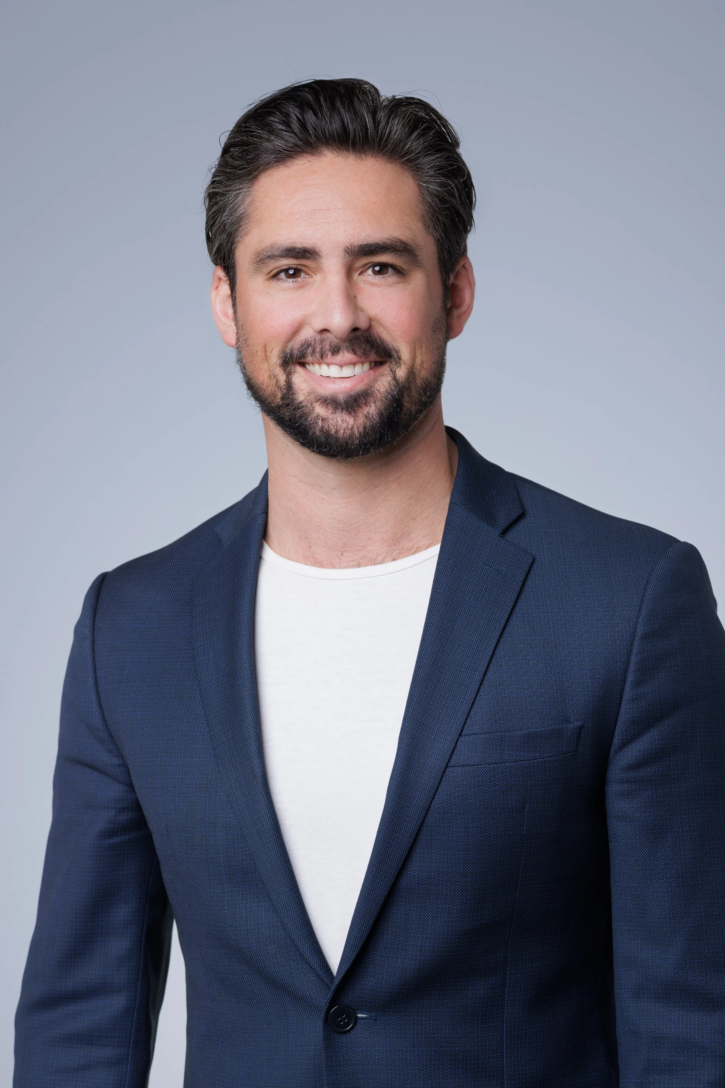 A modern studio portrait by Domain Photography in South Coast Metro, featuring a young professional with a confident, polished presence. The subject is photographed against a clean, minimal backdrop with soft gradient tones, creating a contemporary a