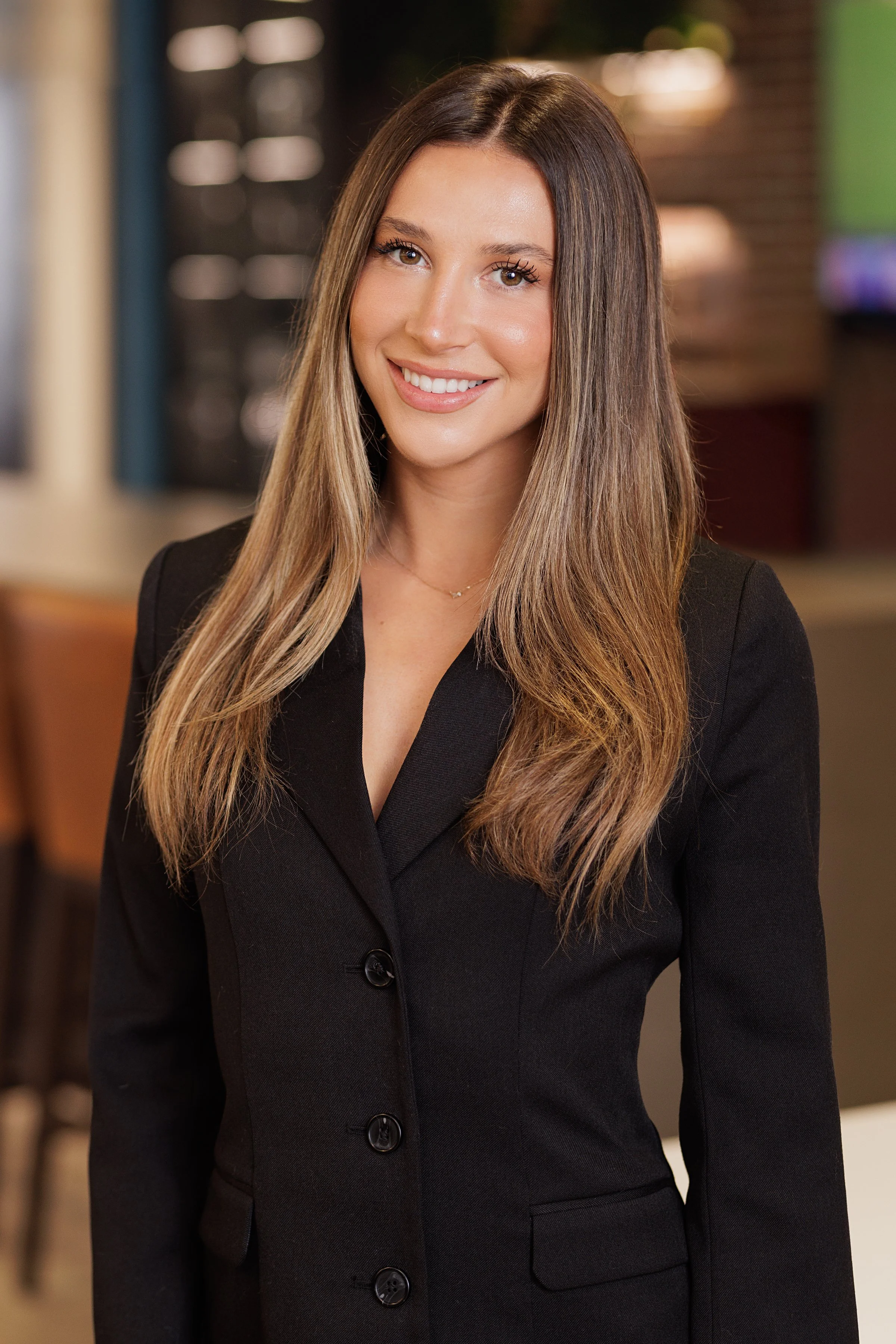 A refined environmental portrait of a young, beautiful professional captured in a modern office setting with a clean, contemporary aesthetic. Floor-to-ceiling windows flood the space with amazing natural light, complemented by subtle professional lig