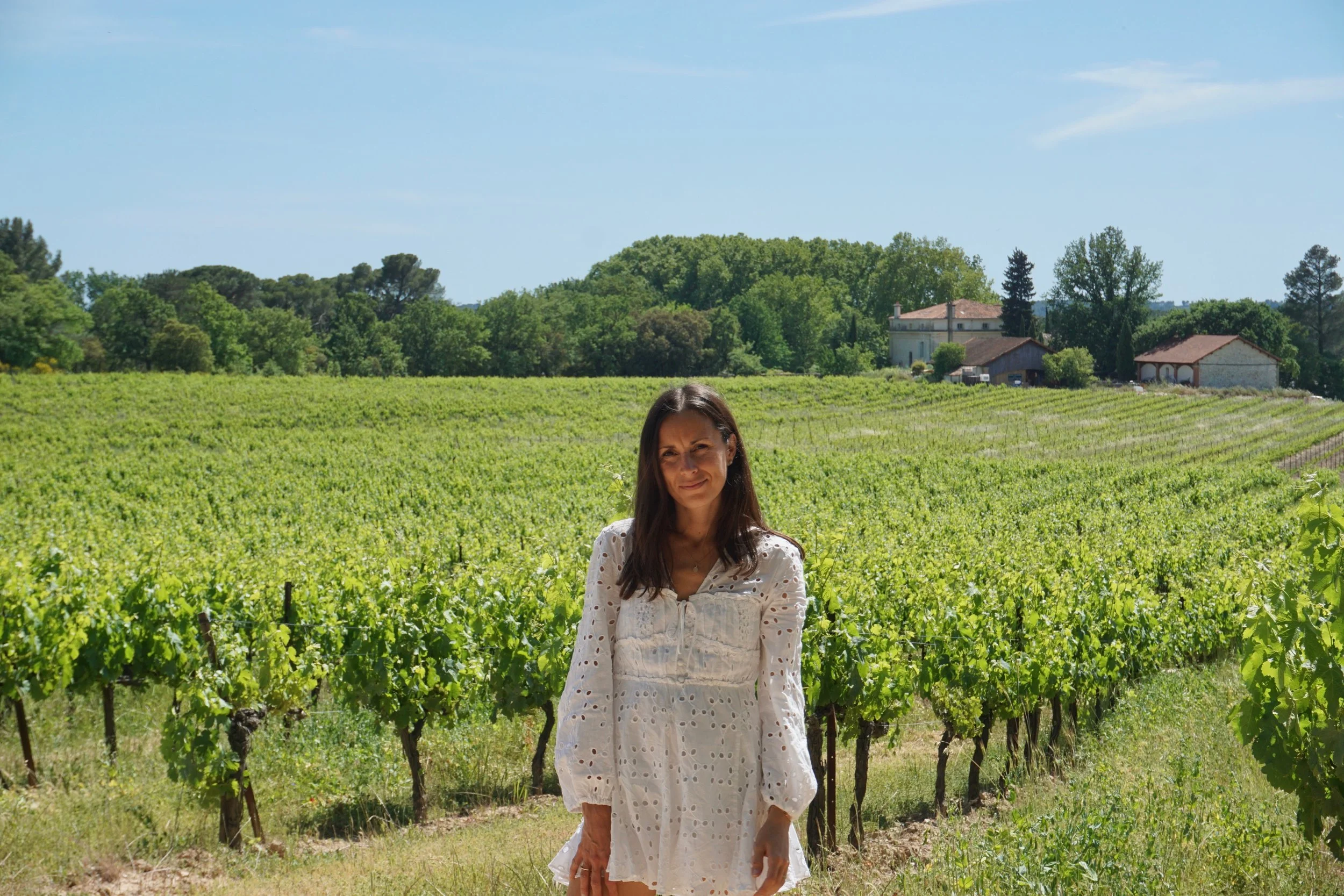 Femme en robe blanche dans un vignoble verdoyant de Provence sous un ciel bleu.
