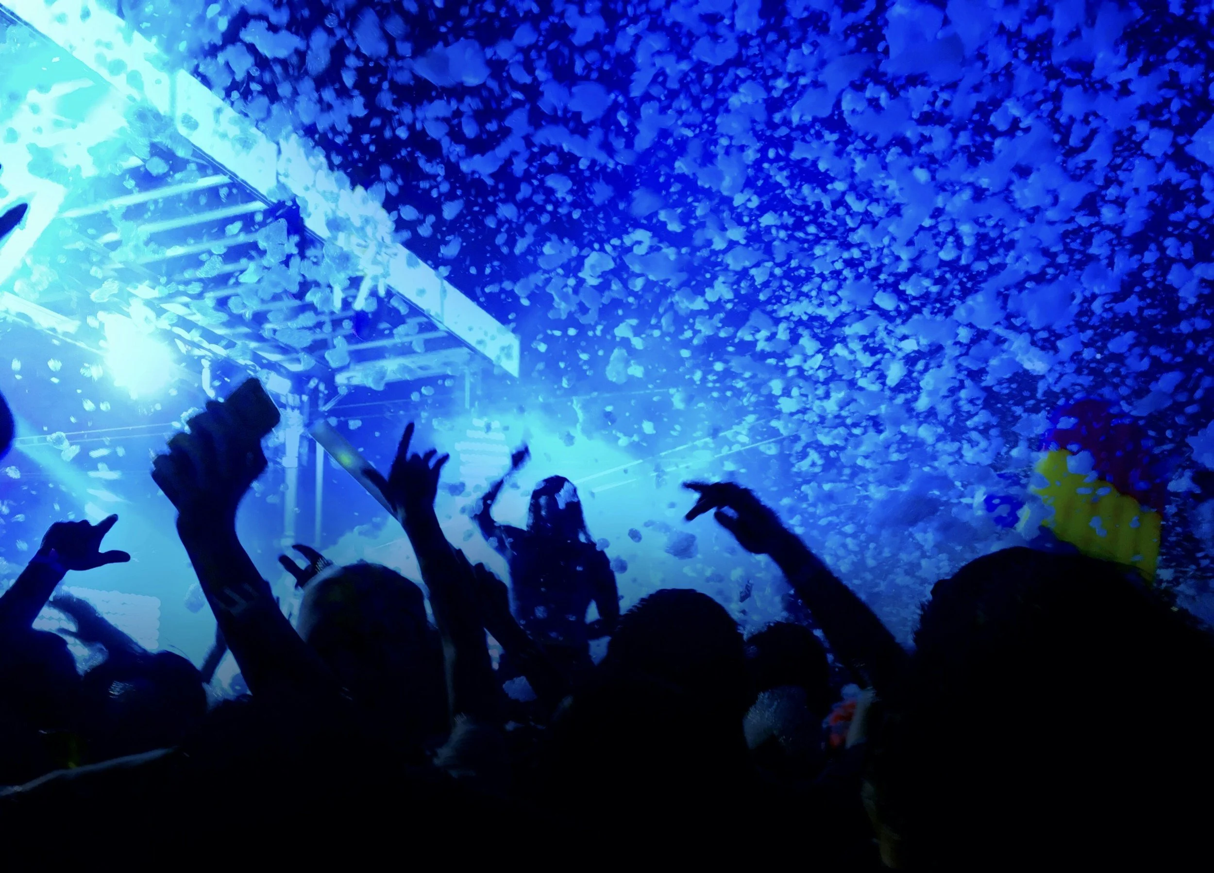 Folk som danser og har det gøy på en nattklubb med blå belysning og konfetti i luften.