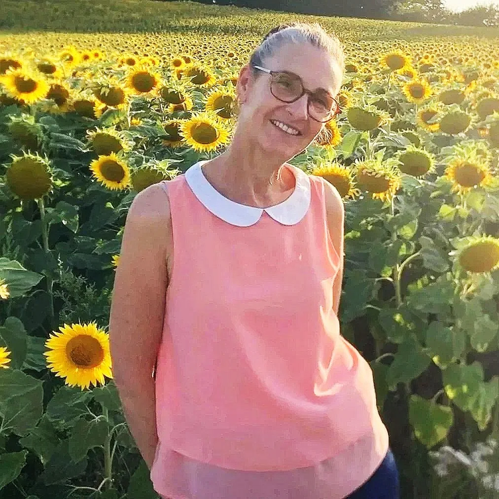 Shirley Kadouri, coach en carrière et en transition, se tient debout dans un champ de tournesols en Suisse, symbole de croissance, de clarté, de confiance et d'authenticité