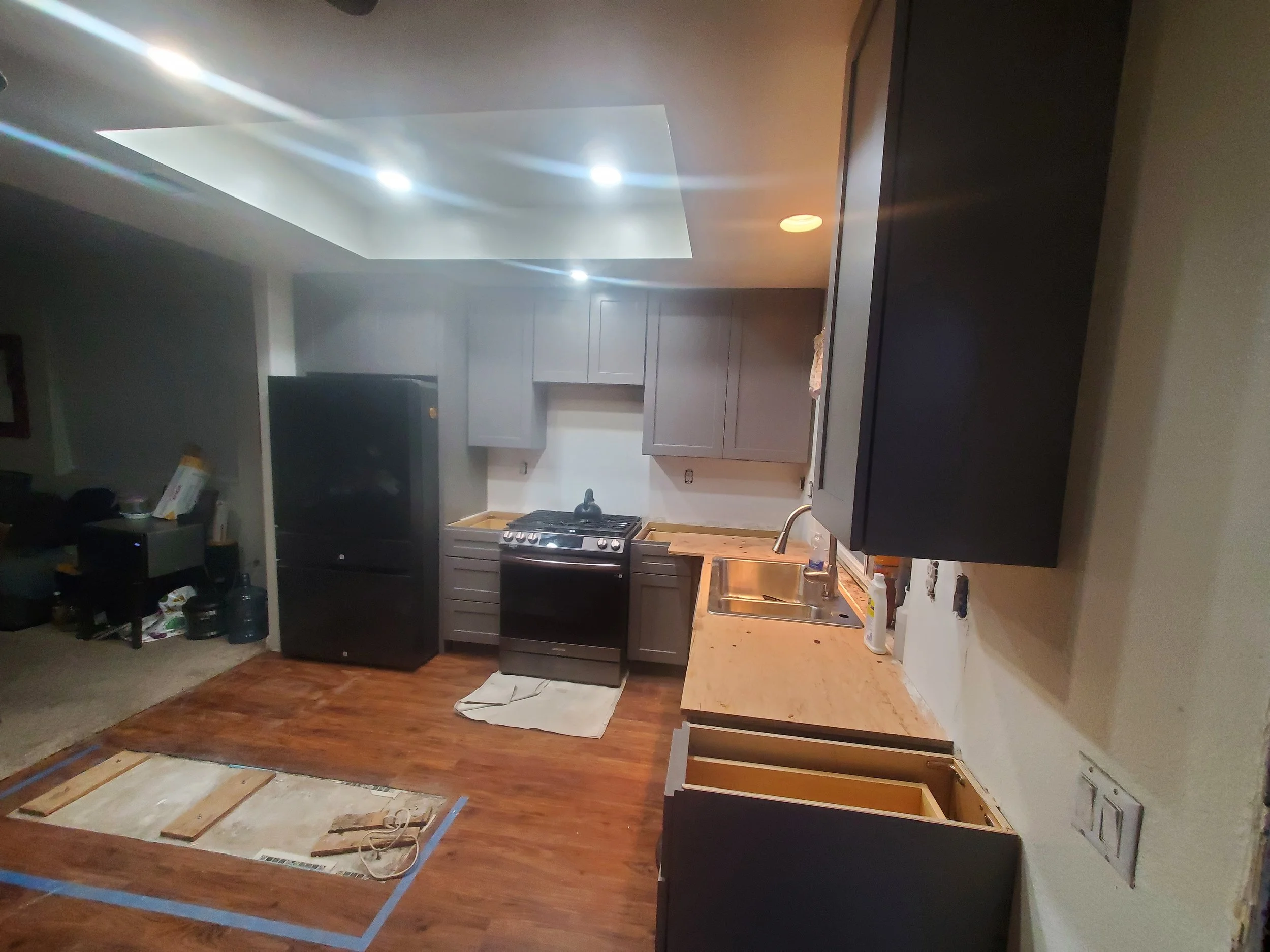 Interior view of a kitchen under renovation with cabinets, oven, and countertop, and flooring work in progress.