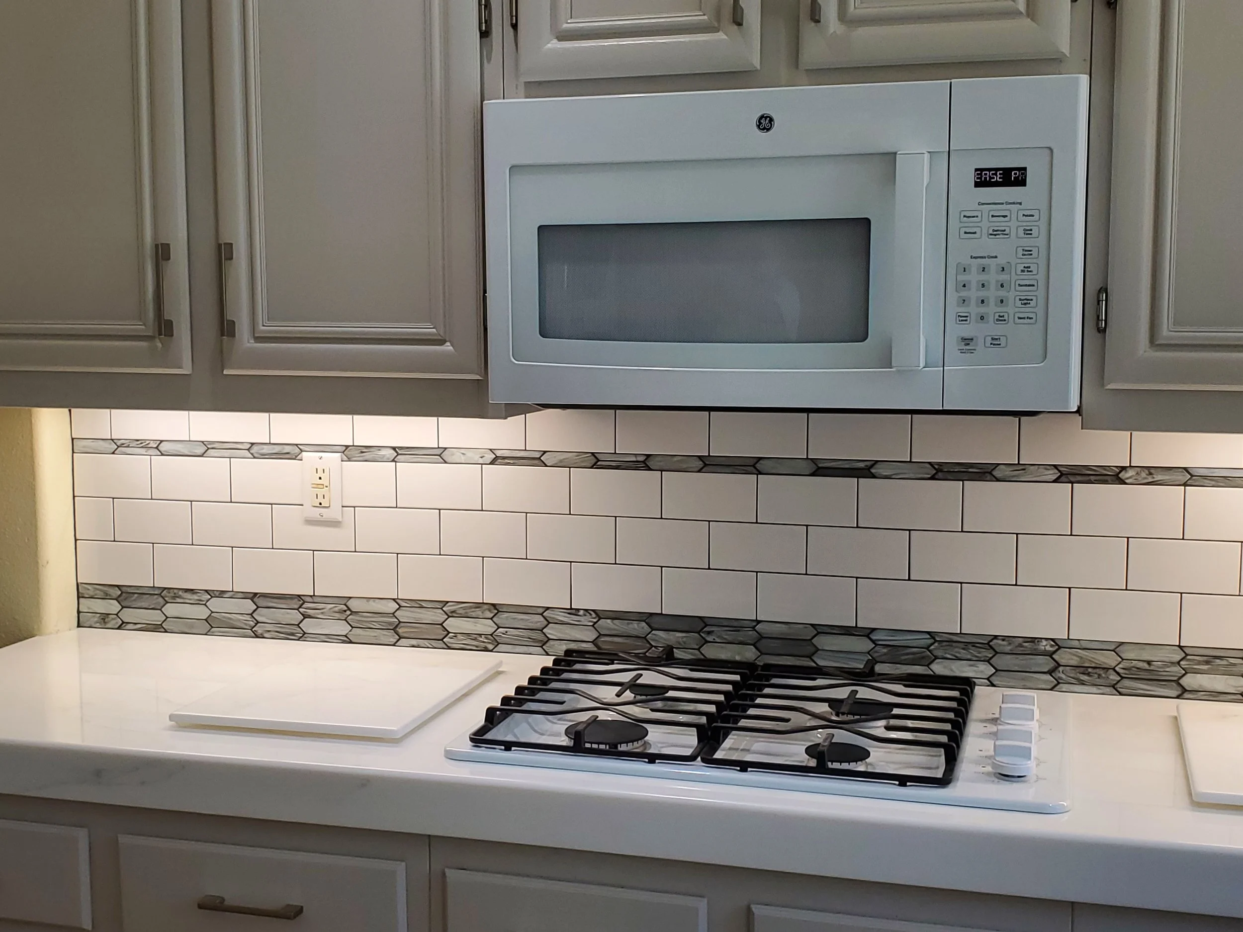 White microwave oven installed above a stove with a four-burner gas cooktop, situated in a kitchen with white cabinets and a tiled backsplash.