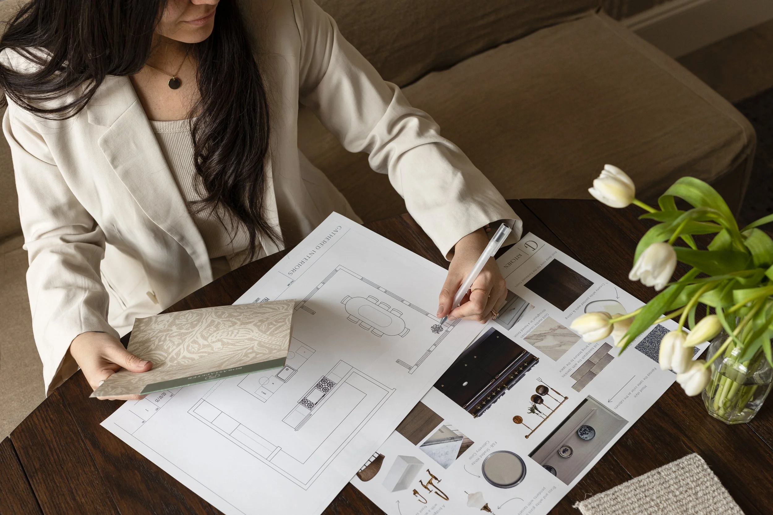 Pam's hand drafting with floor plan and tulips around, cream wallpaper on hand