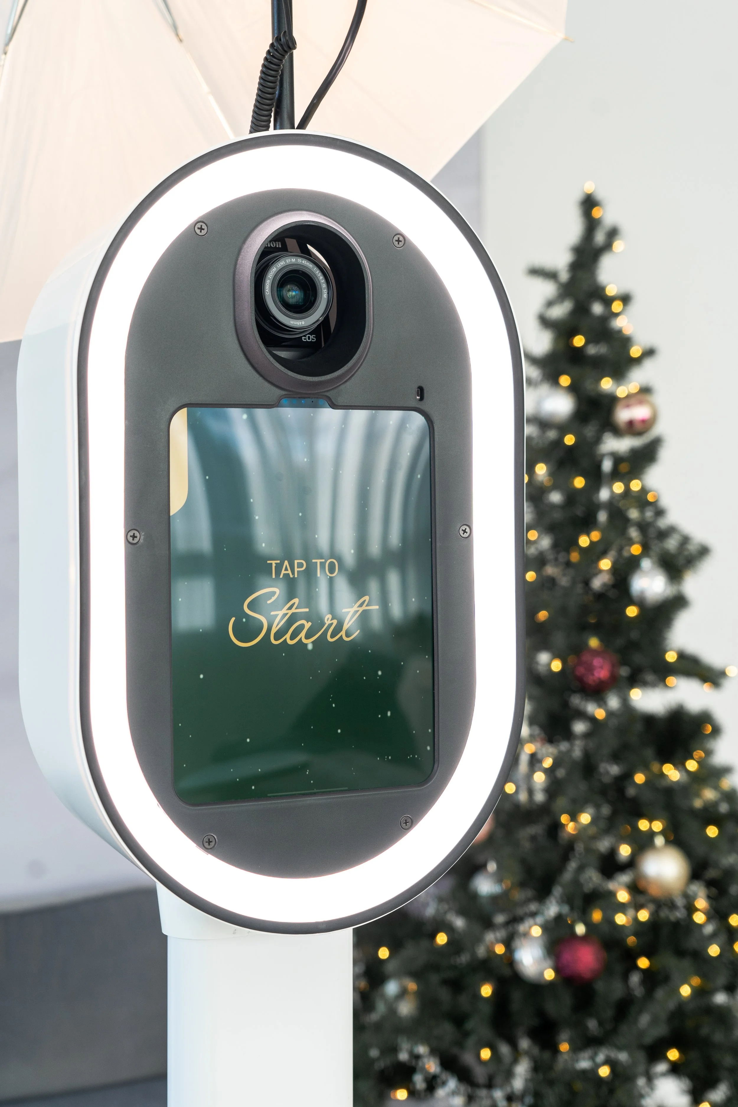 Photo booth with "Tap to Start" on display, Christmas tree with lights and ornaments in the background.