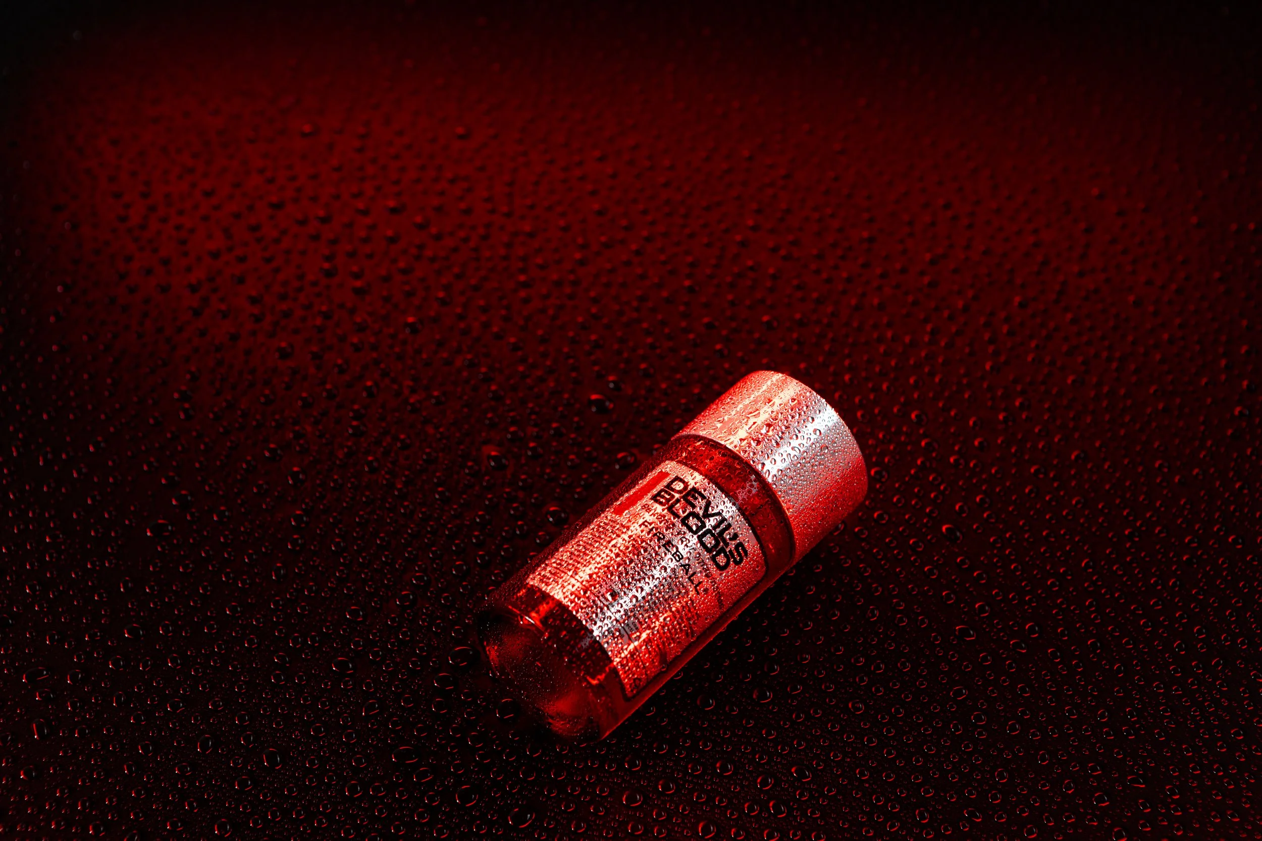 A capsule pill lying on a dark, wet surface with red lighting.