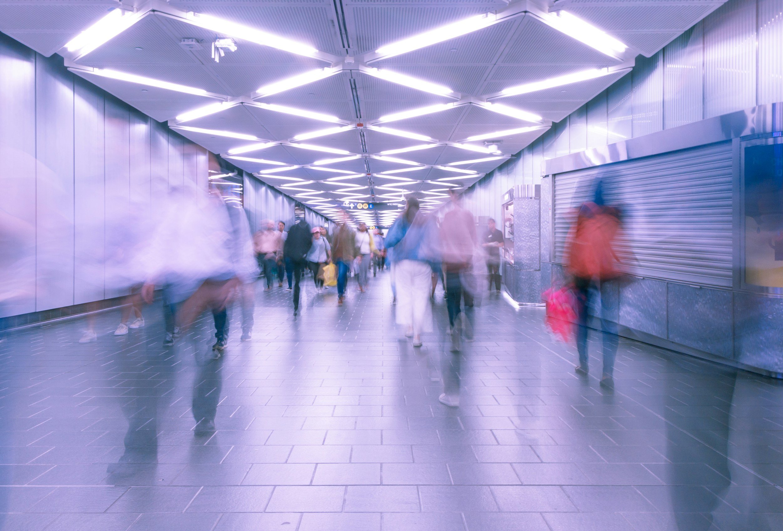 People walking through an underground tunnel with modern ceiling lights in an airport or subway station.