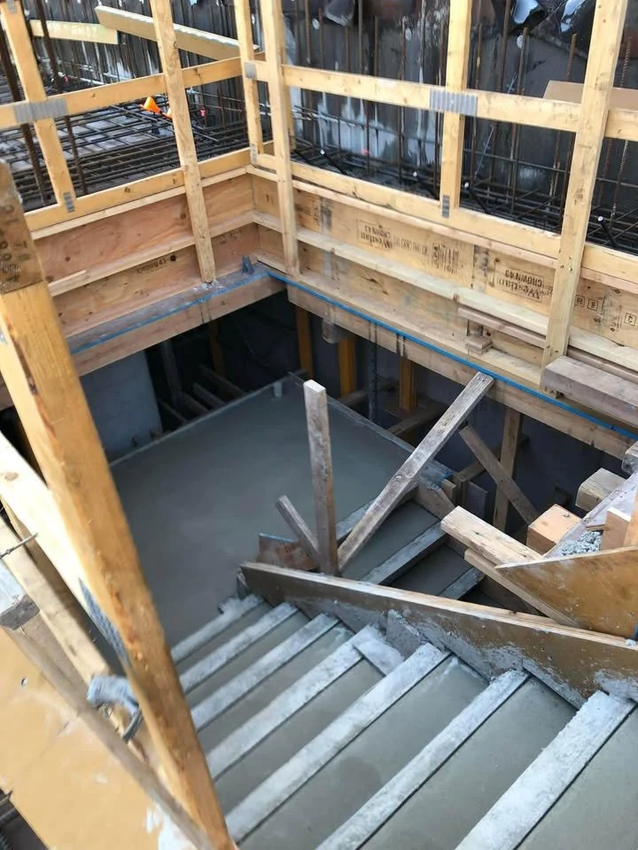 View of a construction site with wooden framing, stairs, and a concrete foundation being poured.