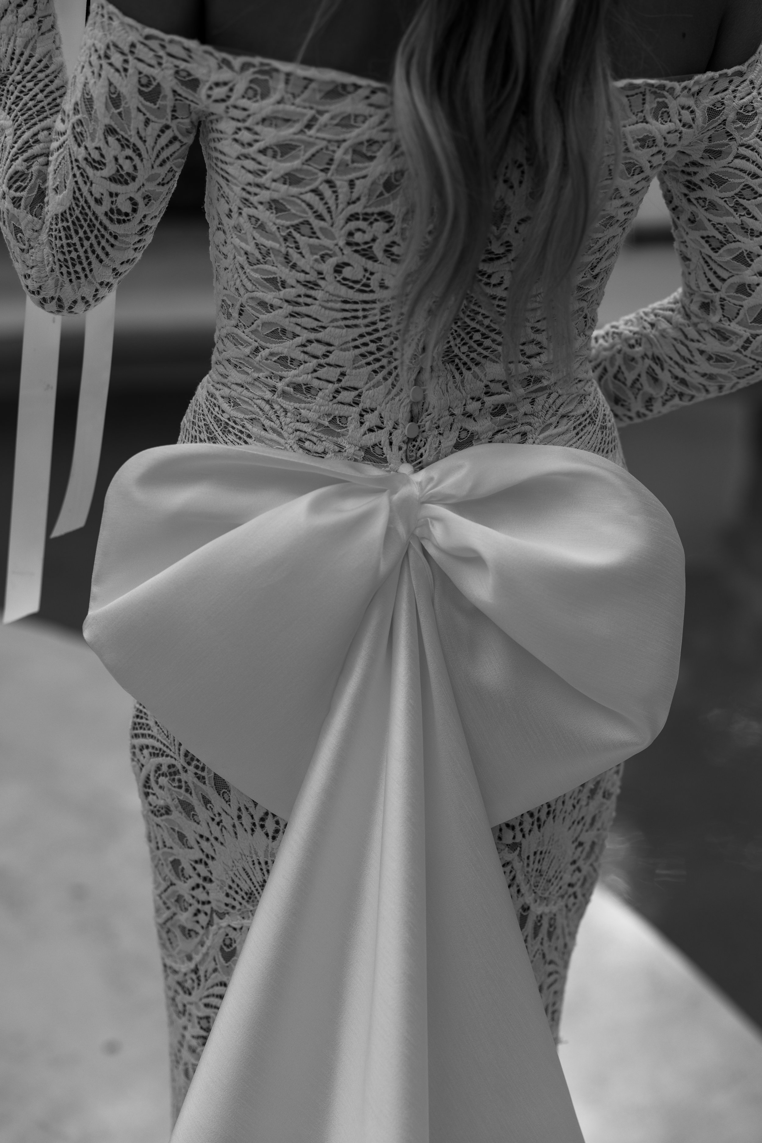 Close-up of a woman wearing a lace dress with an elaborate large satin bow at the waist. Wedding dress, editorial style image. Location Gold Coast Australia
