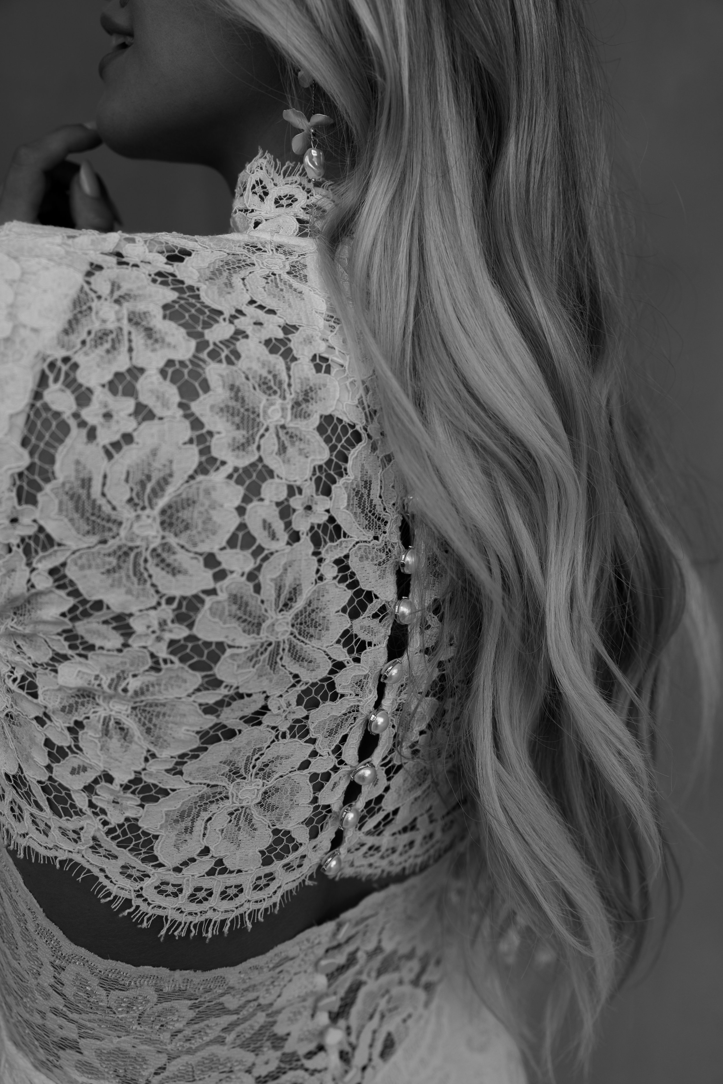 Close-up black and white photo of a woman wearing lace wedding dress and pearl earrings, with wavy hair. Wedding photography, candid moments, Gold Coast Australia