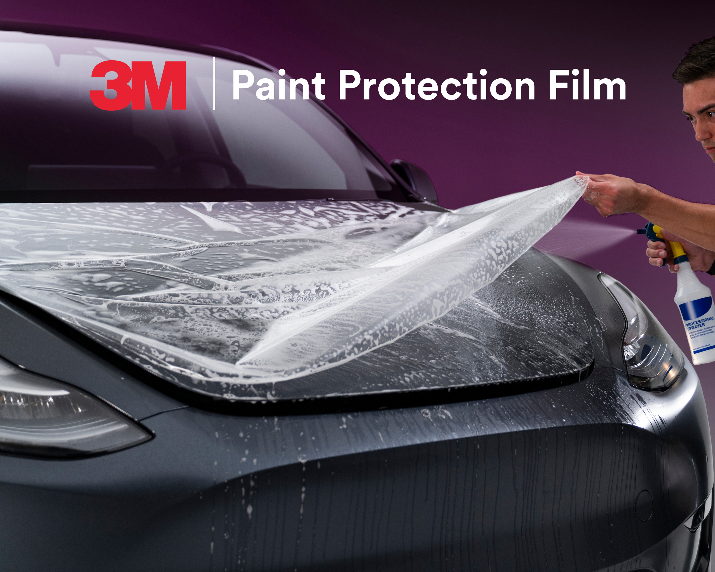 Person applying protective film to a car window, holding a spray bottle