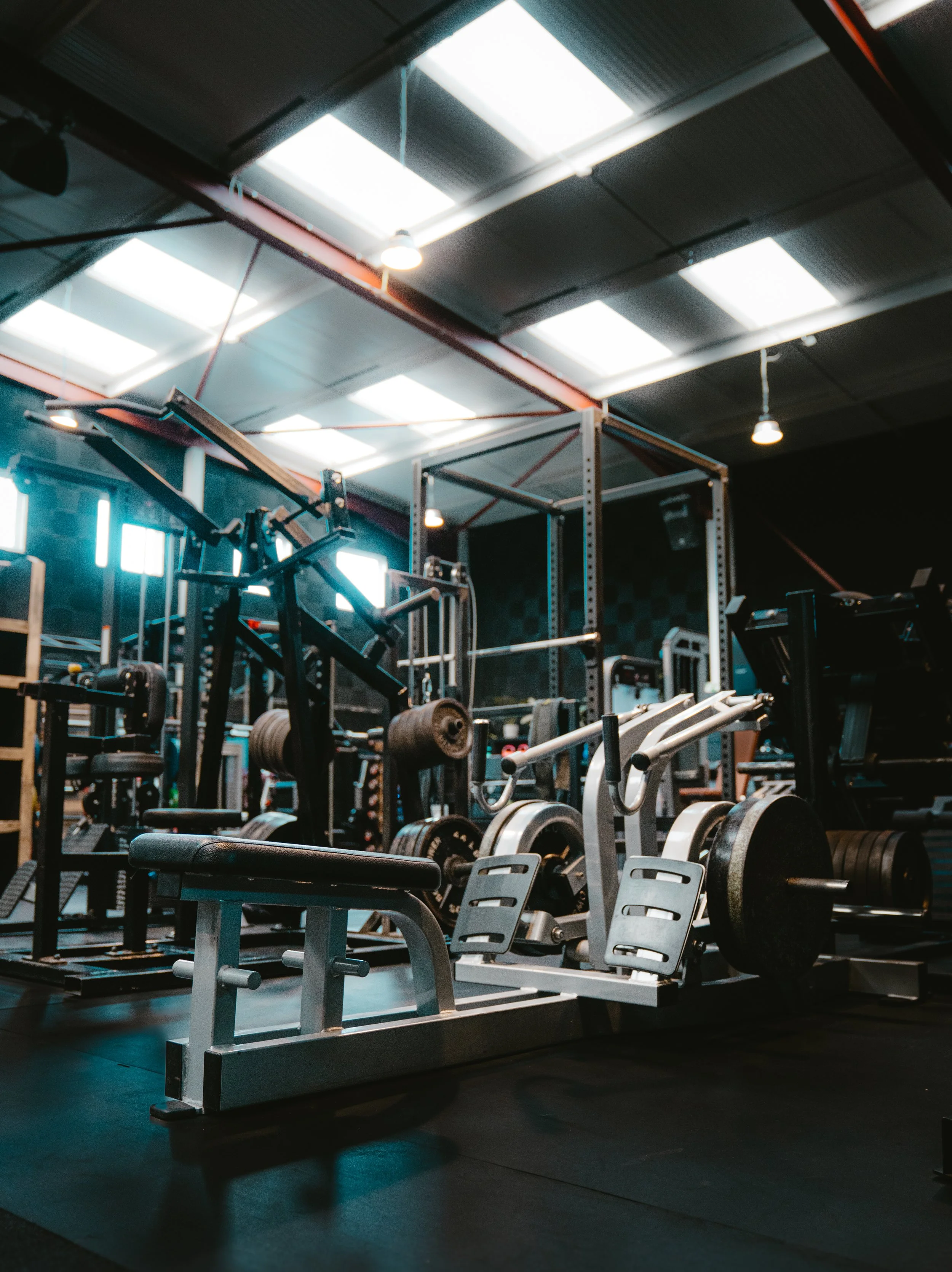 Empty gym with weightlifting equipment, including a bench, weight plates, and a power rack, in a modern workout space.