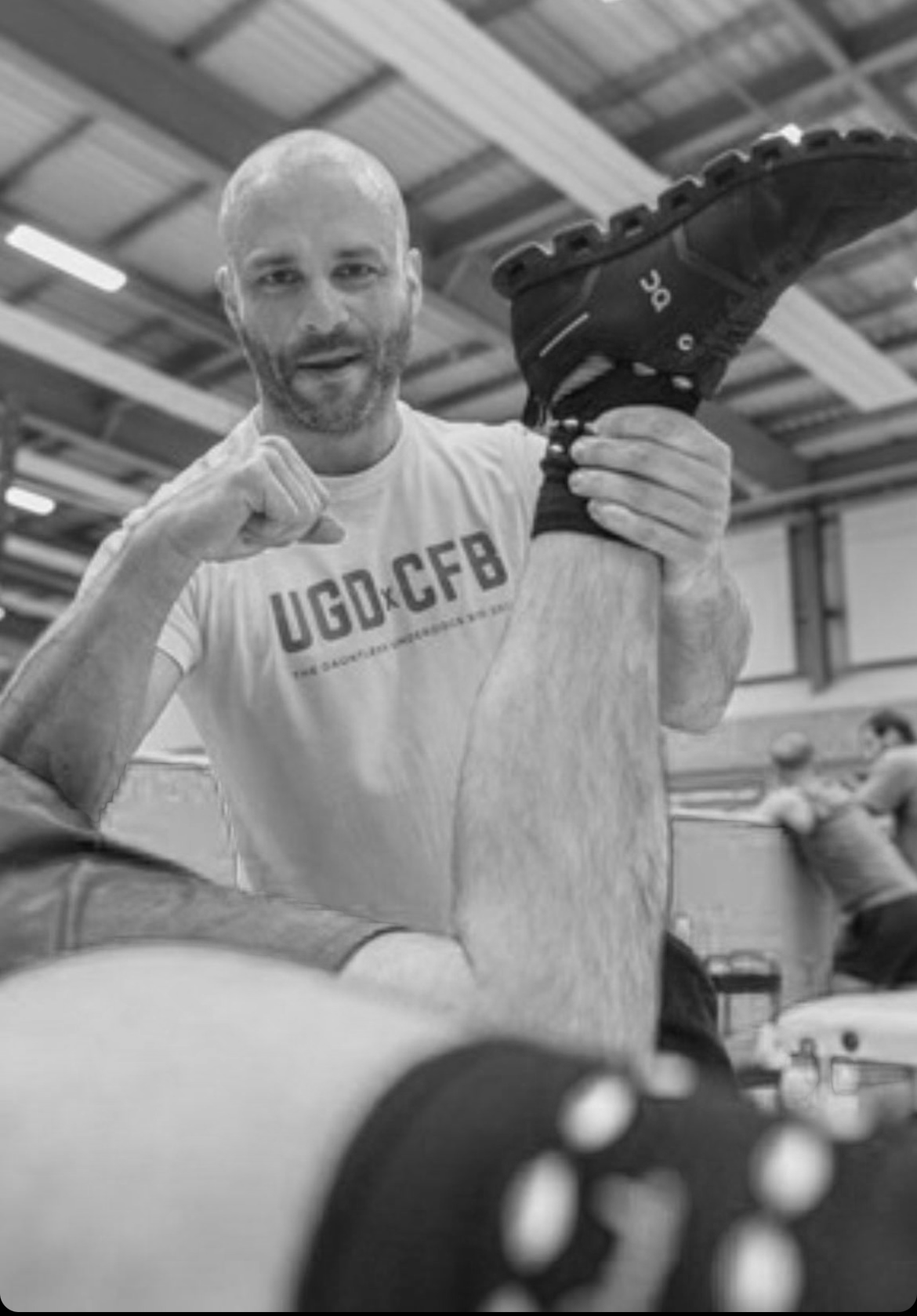 A muscular man performing a piriformis release on an athlete at a fitness event, in a black-and-white photo.