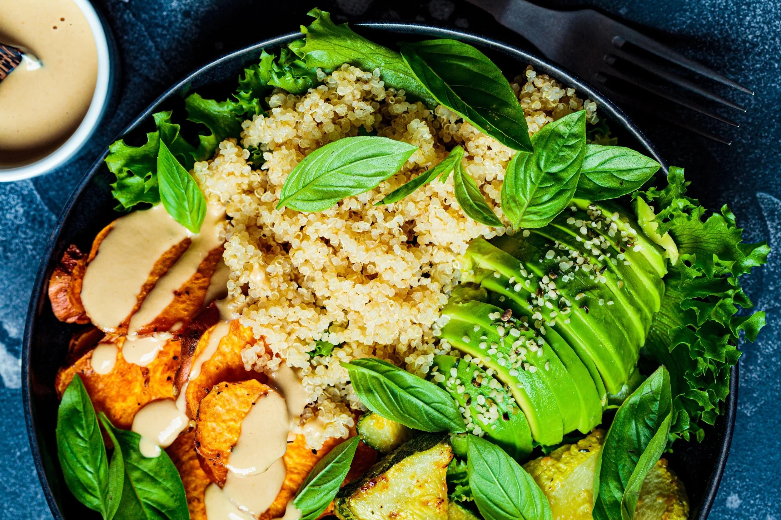 Een salade met geitenkaas, avocadoplakjes, quinoa, sla en basilicumblaadjes, met een apart schaaltje honing of mosterd saus.