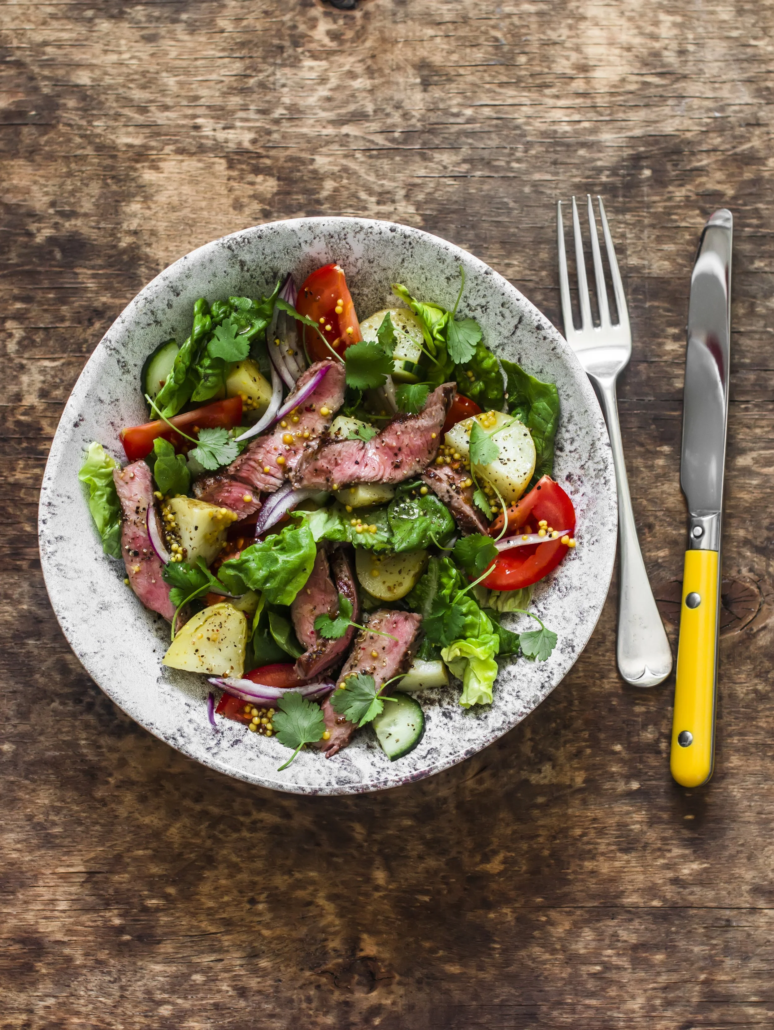 Een bord met verse salade met radijs, komkommer, walnoten en plakjes vlees op een donkere achtergrond.
