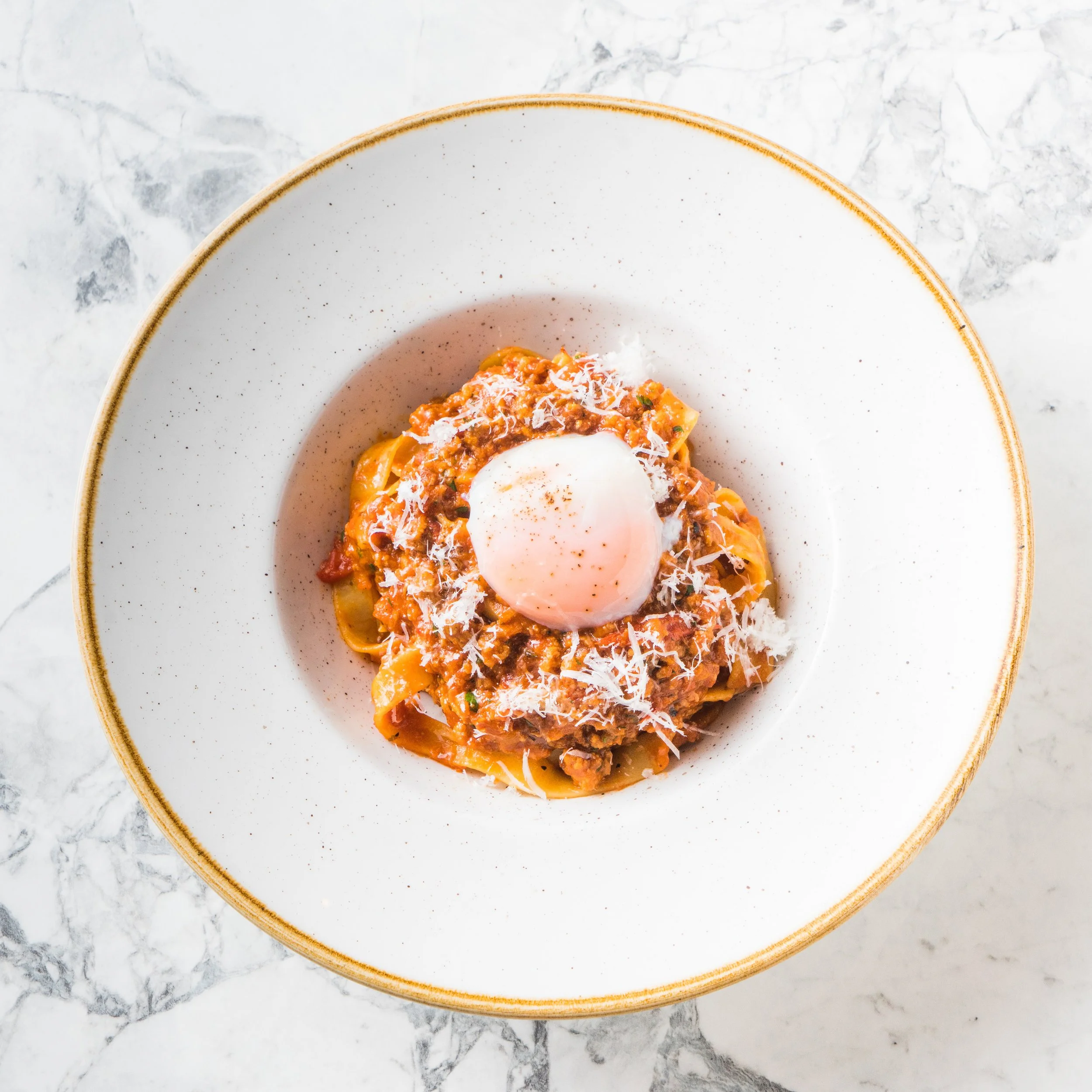 Bord met pasta met een vlees- en tomatensaus, geserveerd met een gepocheerd ei en geraspte kaas