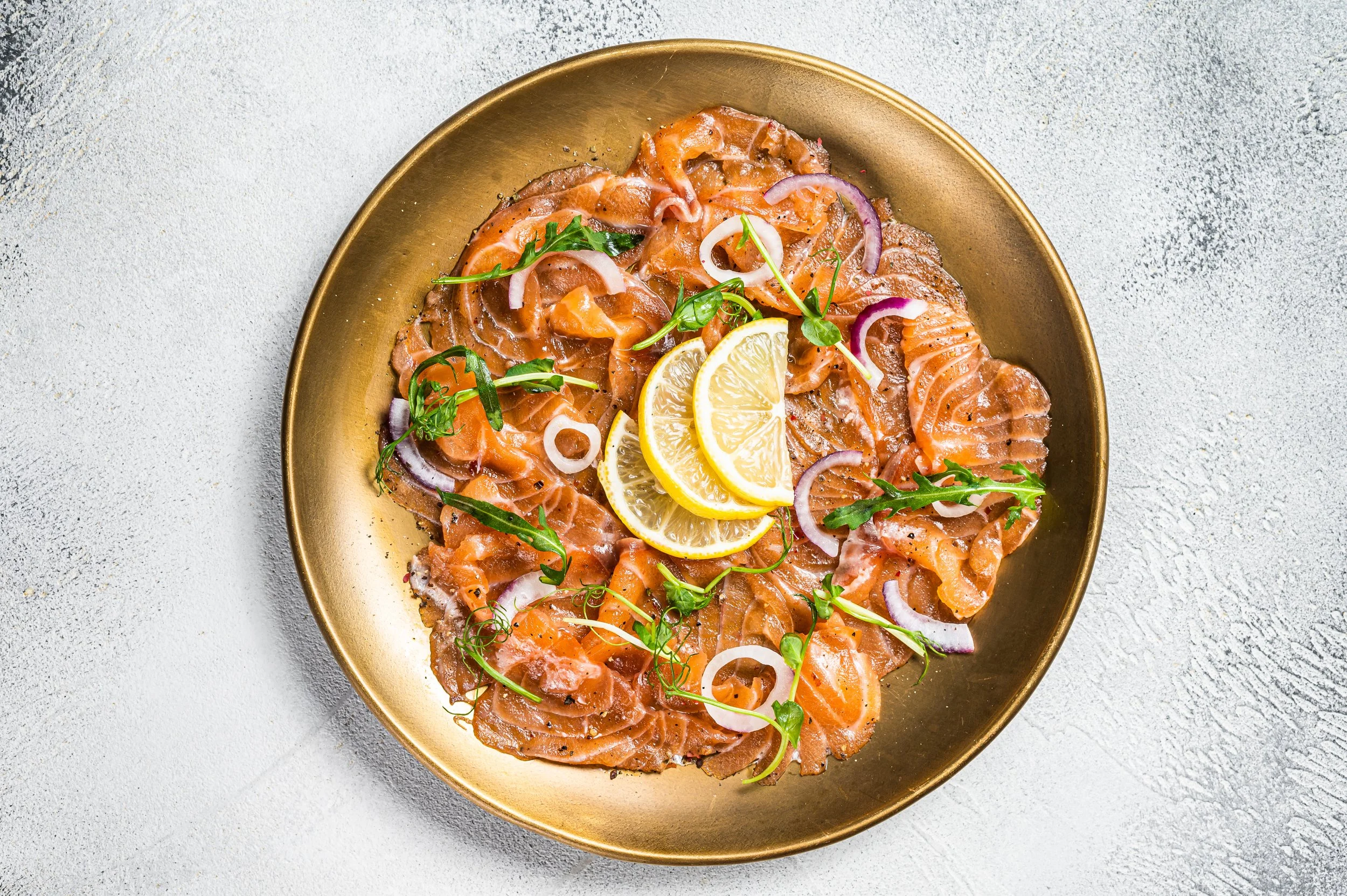 Gerookte zalm met citroen, rode ui, kappertjes en rucola op een gouden bord