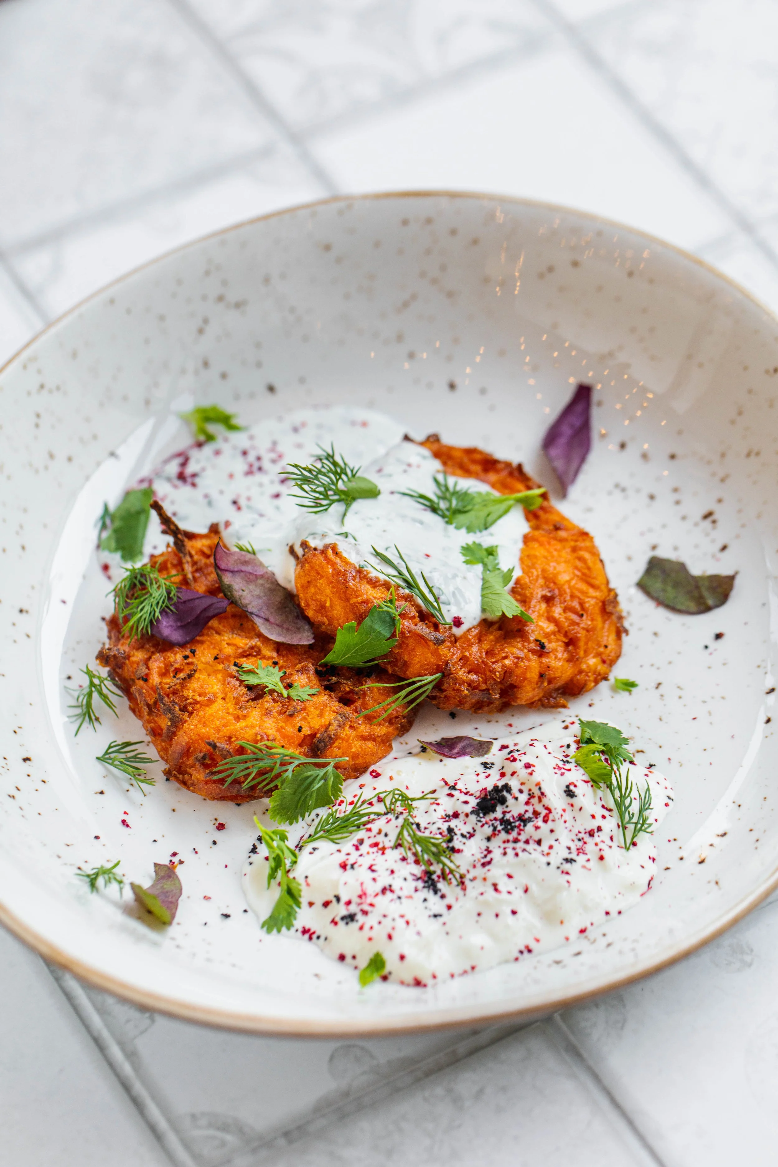 Gebakken vis met zure roomsaus en verse kruiden op een wit bord.