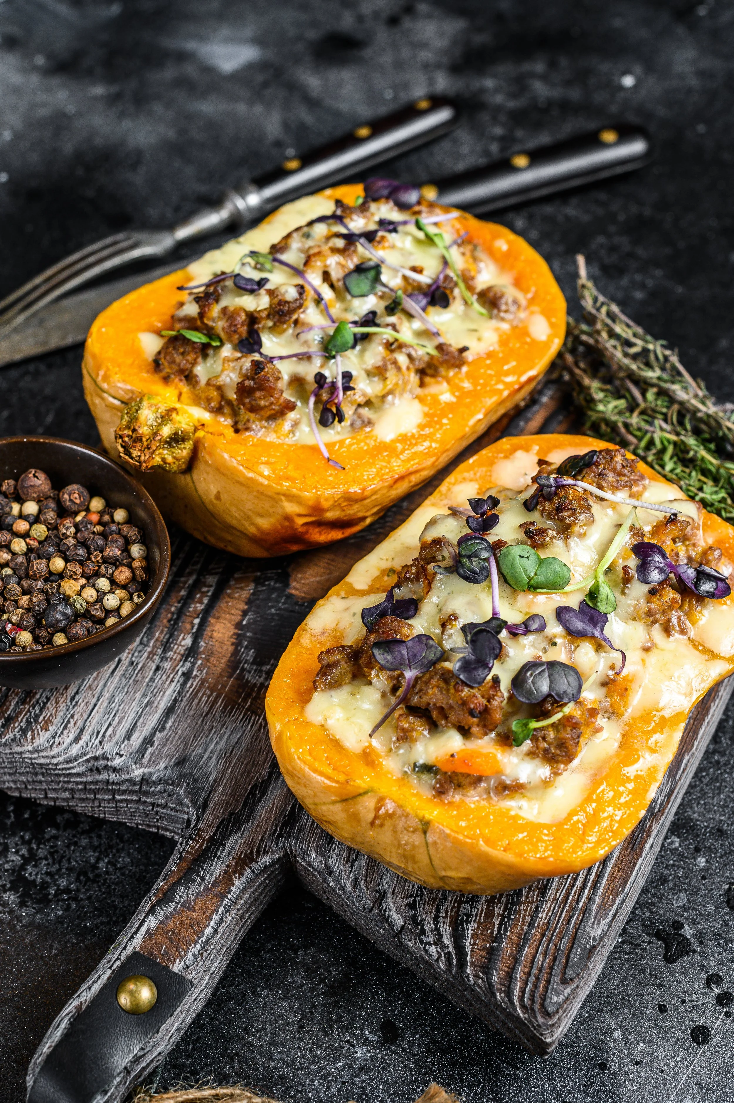 Gevulde butternut squash met kaas, gehakt en microgroenten op een houten snijplank.