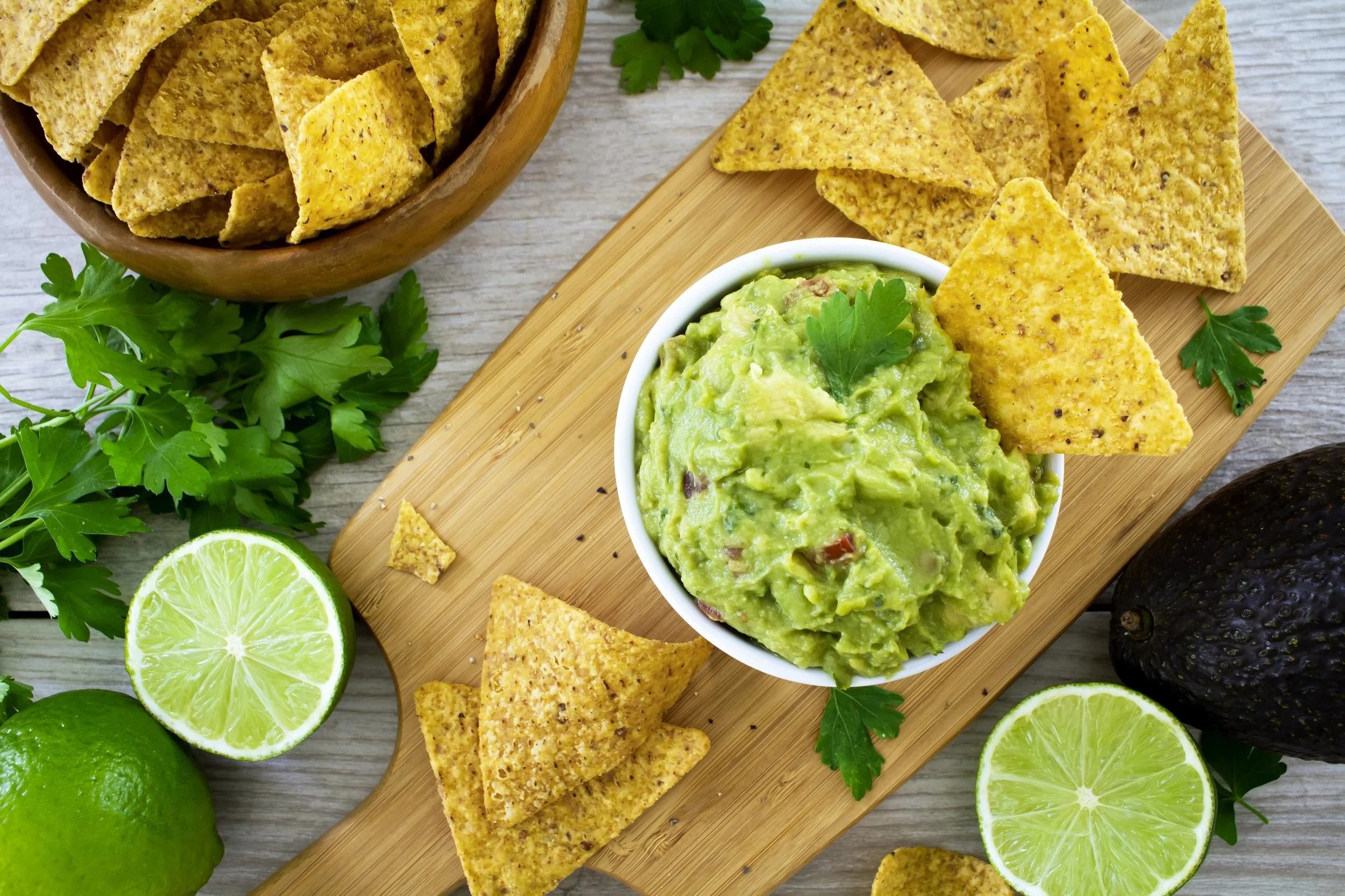 Borden met avocado dip, tortillachips, limoenen, verse koriander en een kom met tortillachips.
