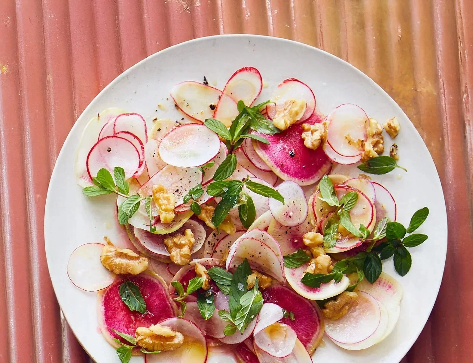 Sla, radijs, walnoten, muntblaadjes en peper op een wit bord