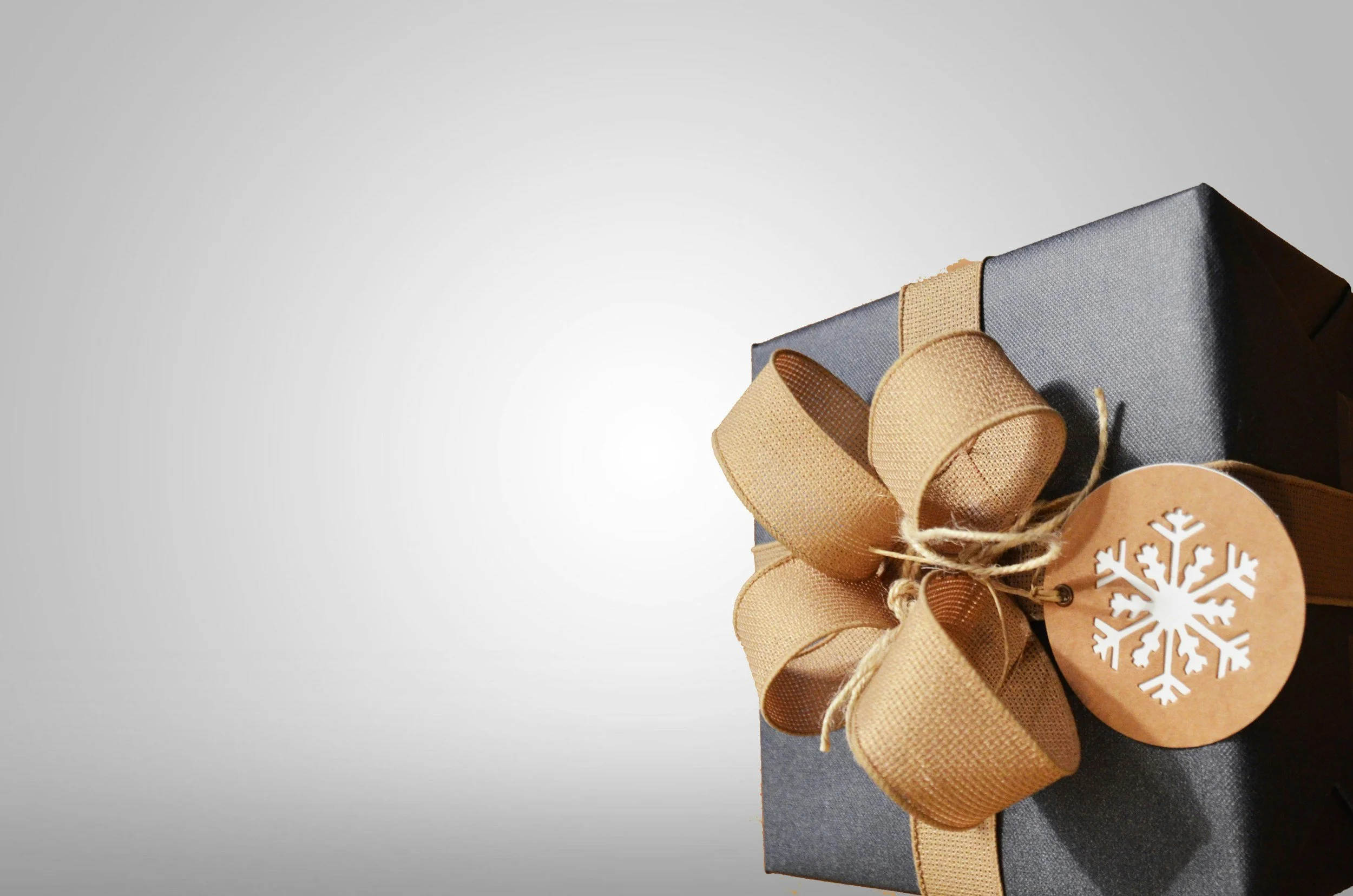 Black gift box with a brown ribbon and snowflake tag on a gray background.