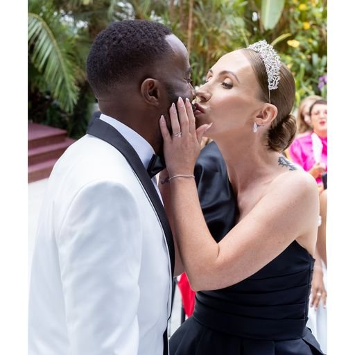 Bride and groom sharing a tender kiss at a wedding with greenery in the background.