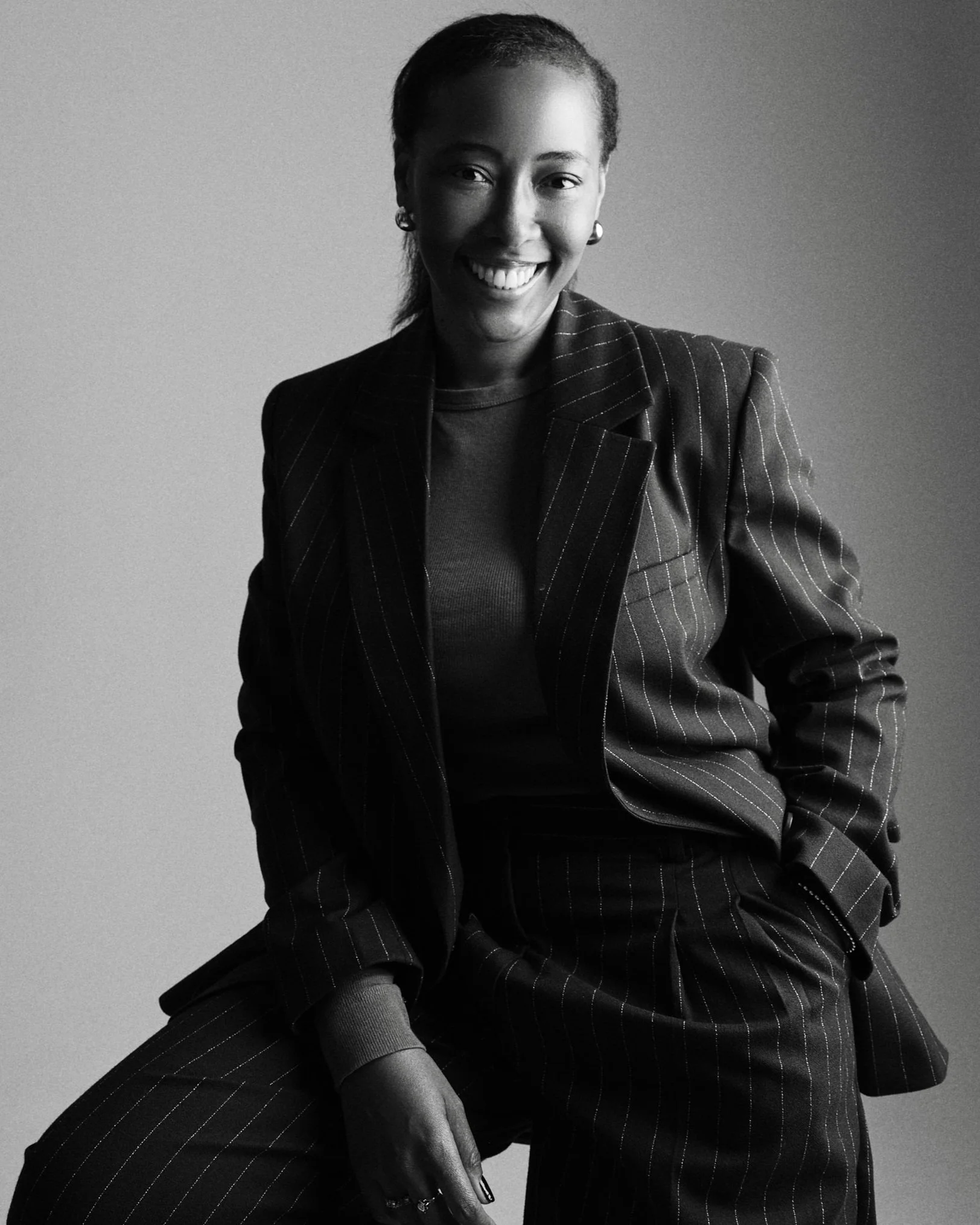Black and white portrait of a smiling woman in a pinstripe suit, sitting against a plain background.
