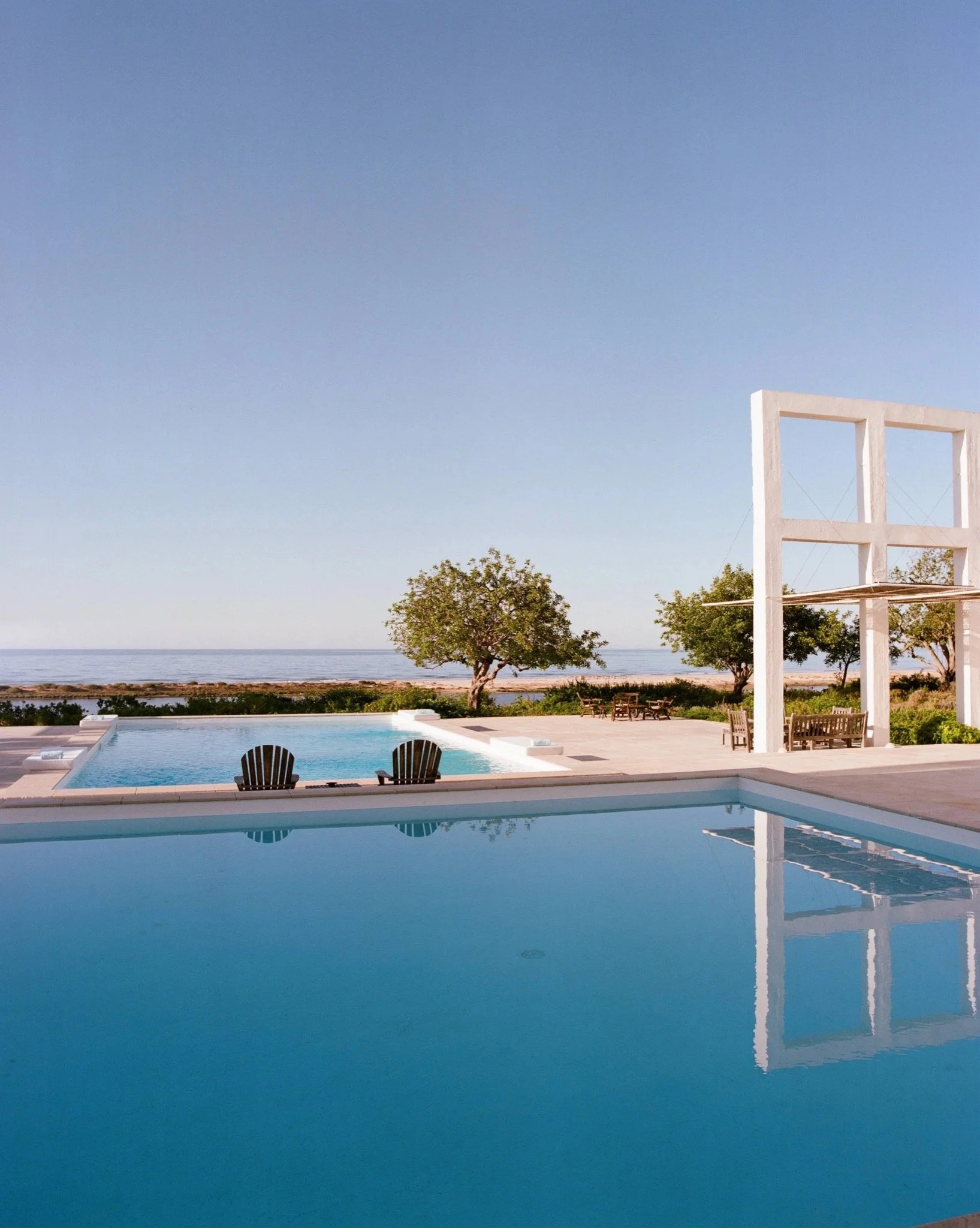 Infinity pool and sea-facing terrace framed by white architectural structures at Quinta do Muro in Portugal.