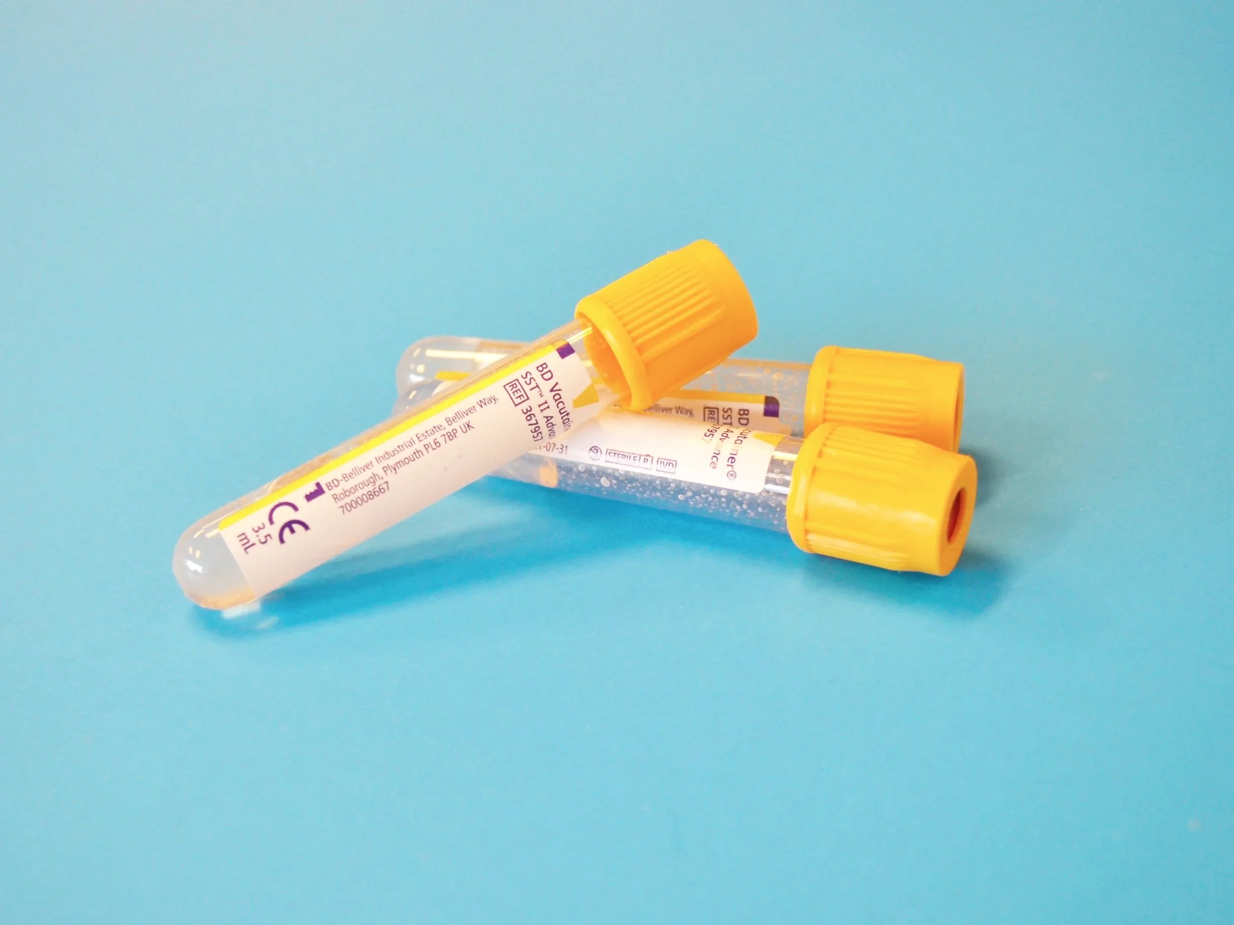 Three transparent test tubes with yellow caps lying on a blue surface, with labels and some liquid inside.