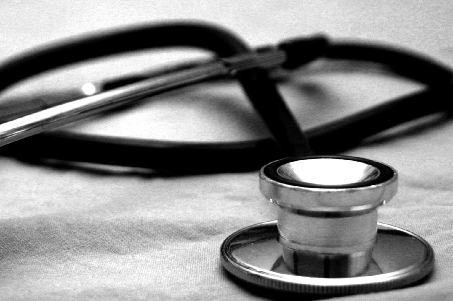 Black and white close-up of a stethoscope lying on a medical surface.