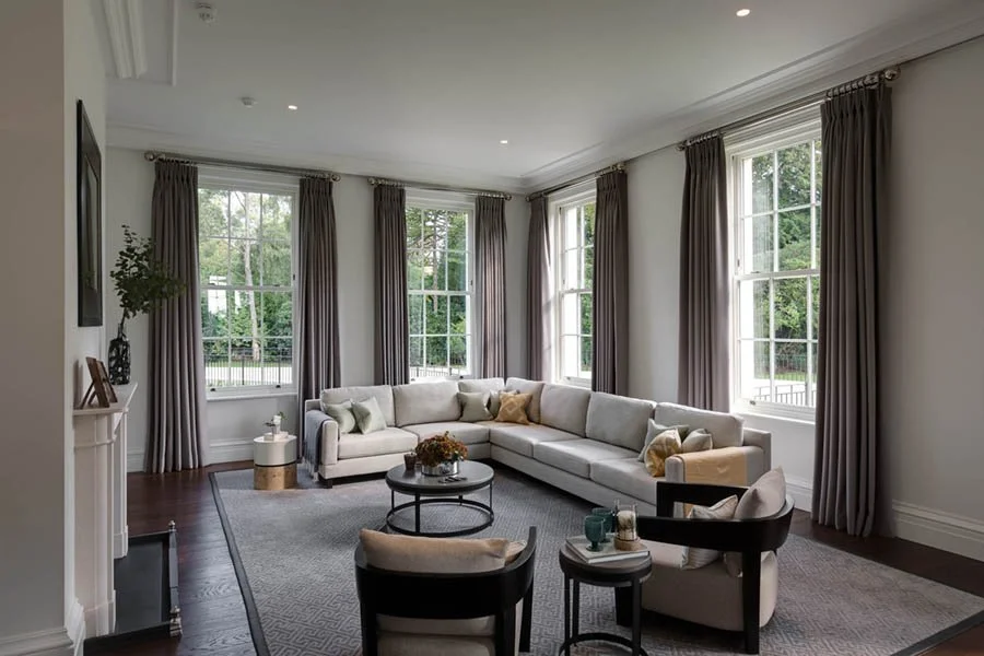 LA London Architects LLP — Living room with a large sectional sofa, window with curtains, armchairs, and a coffee table.