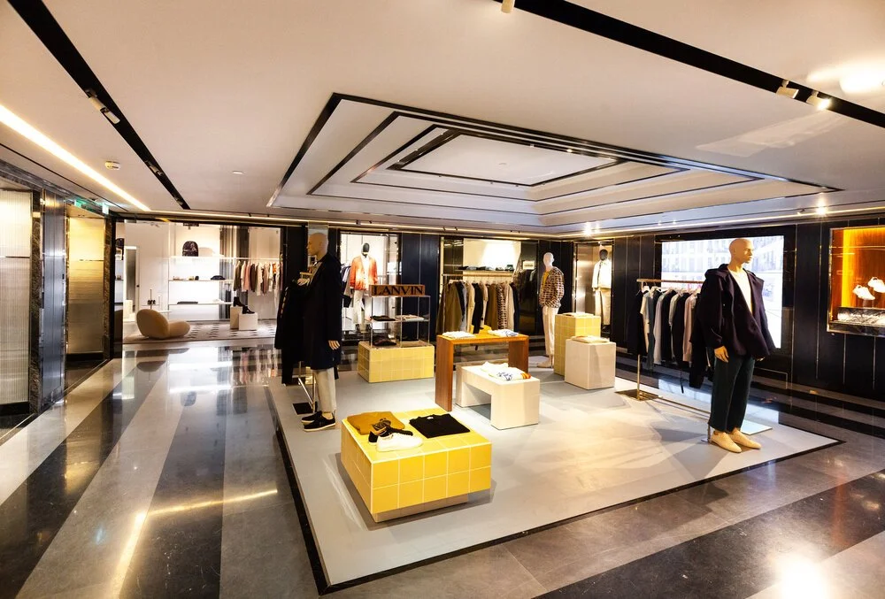 LA London Architects LLP — Interior of a clothing store with mannequins displaying apparel, shelves with handbags, and racks of clothing, with modern lighting and design.
