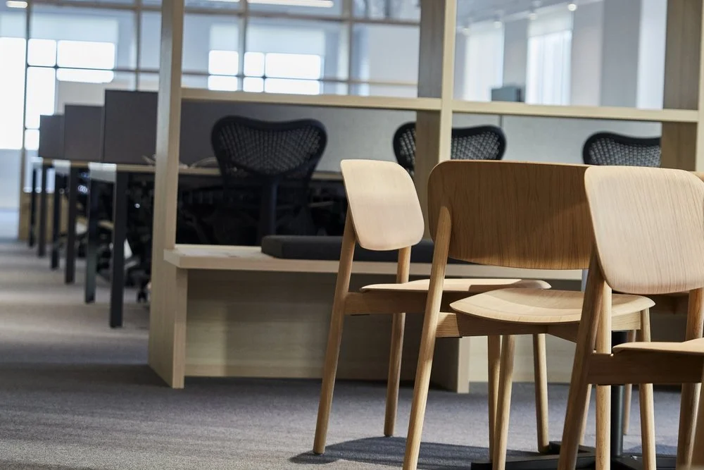 LA London Architects LLP — Empty office space with wooden chairs, desks, and black mesh office chairs near windows.