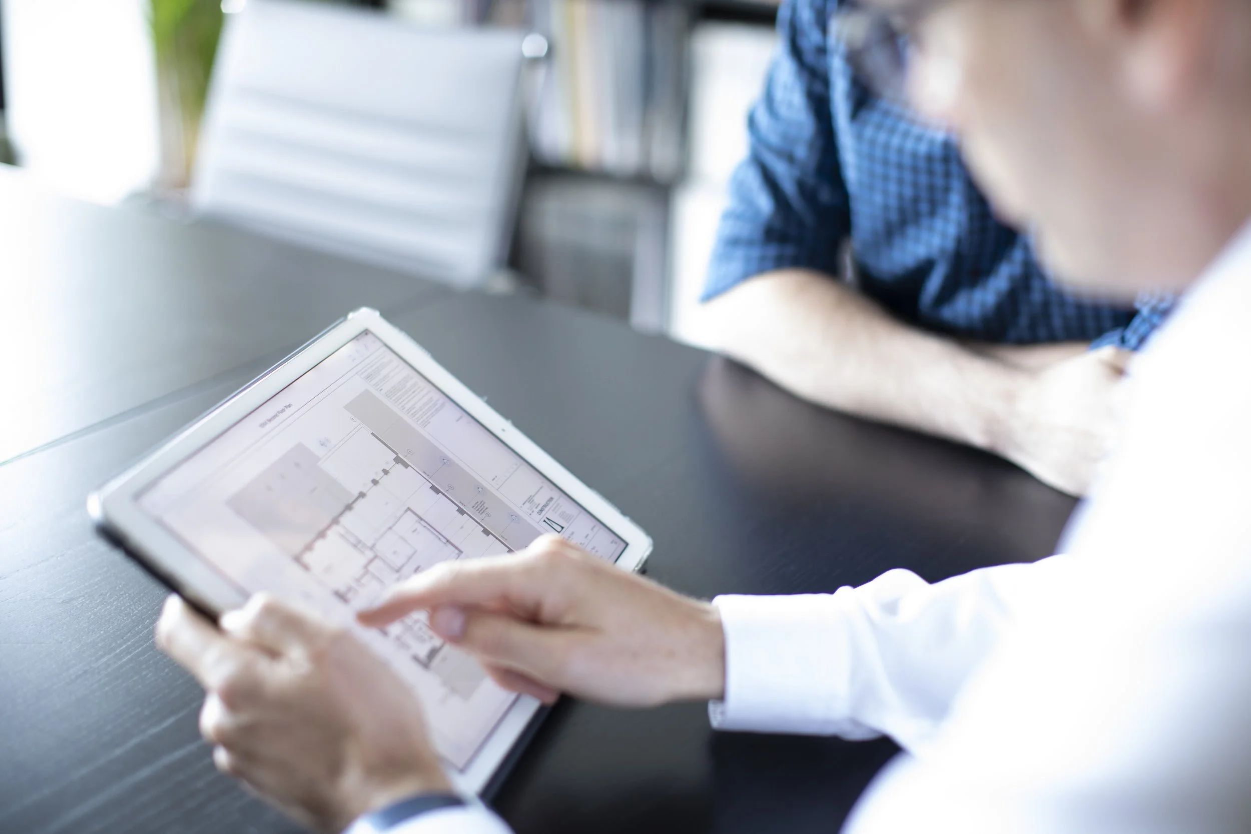 Person analyzing a digital building floor plan on a tablet during a business meeting.