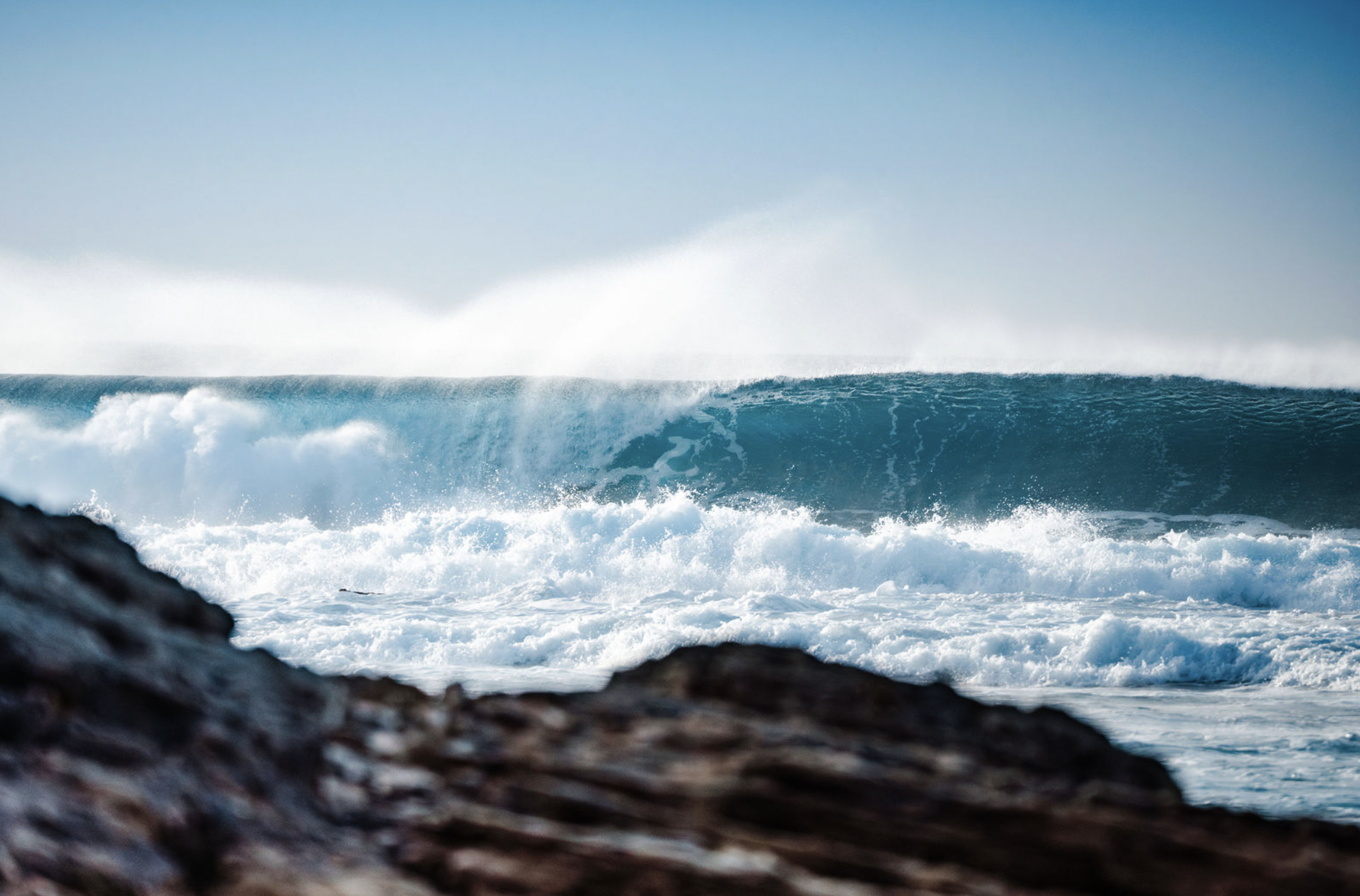 Ocean waves crashing against rocks with a clear blue sky in the background.