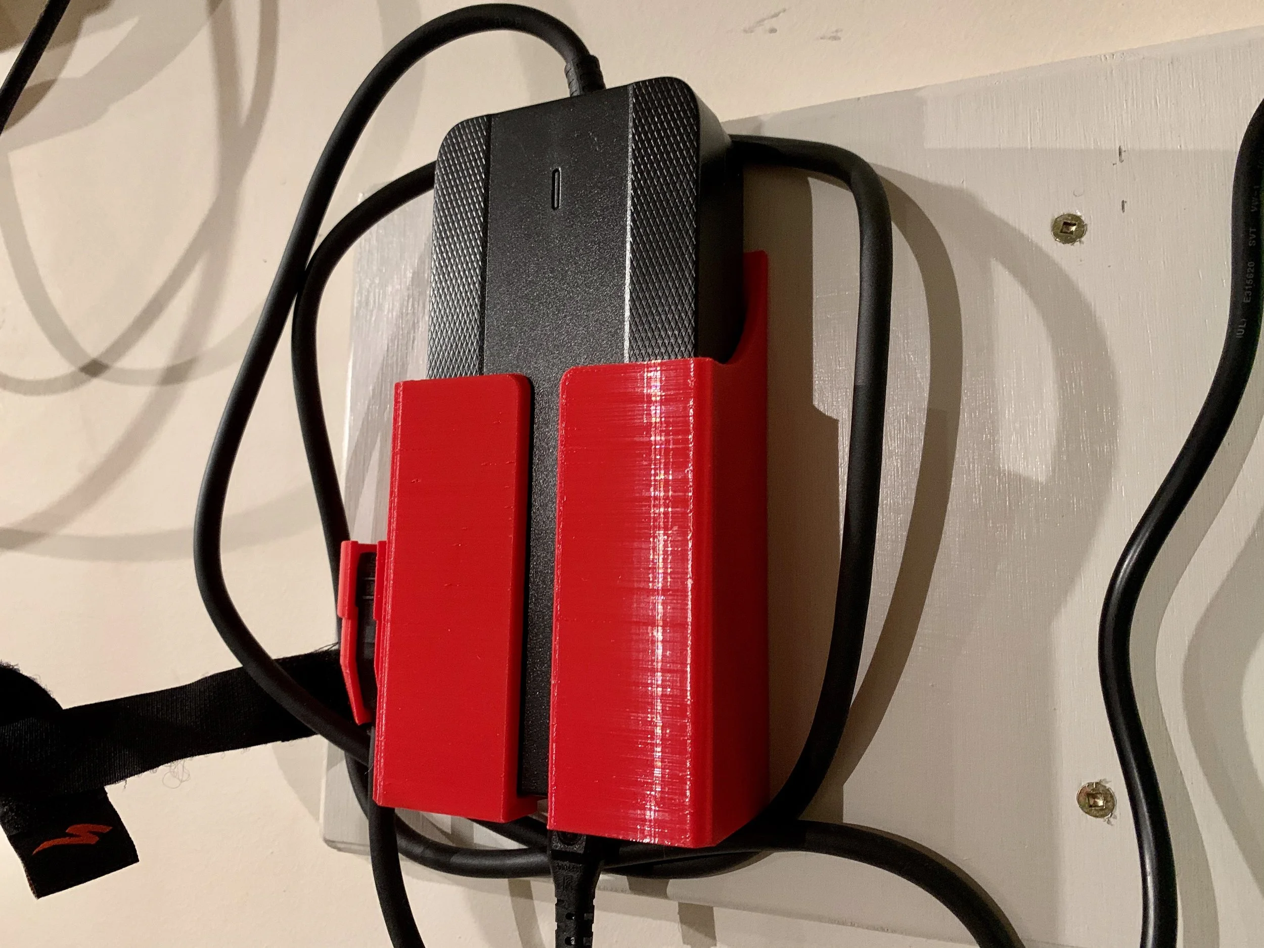 A small black electronic device connected to several cables mounted on a wall, with a red 3D-printed holder.