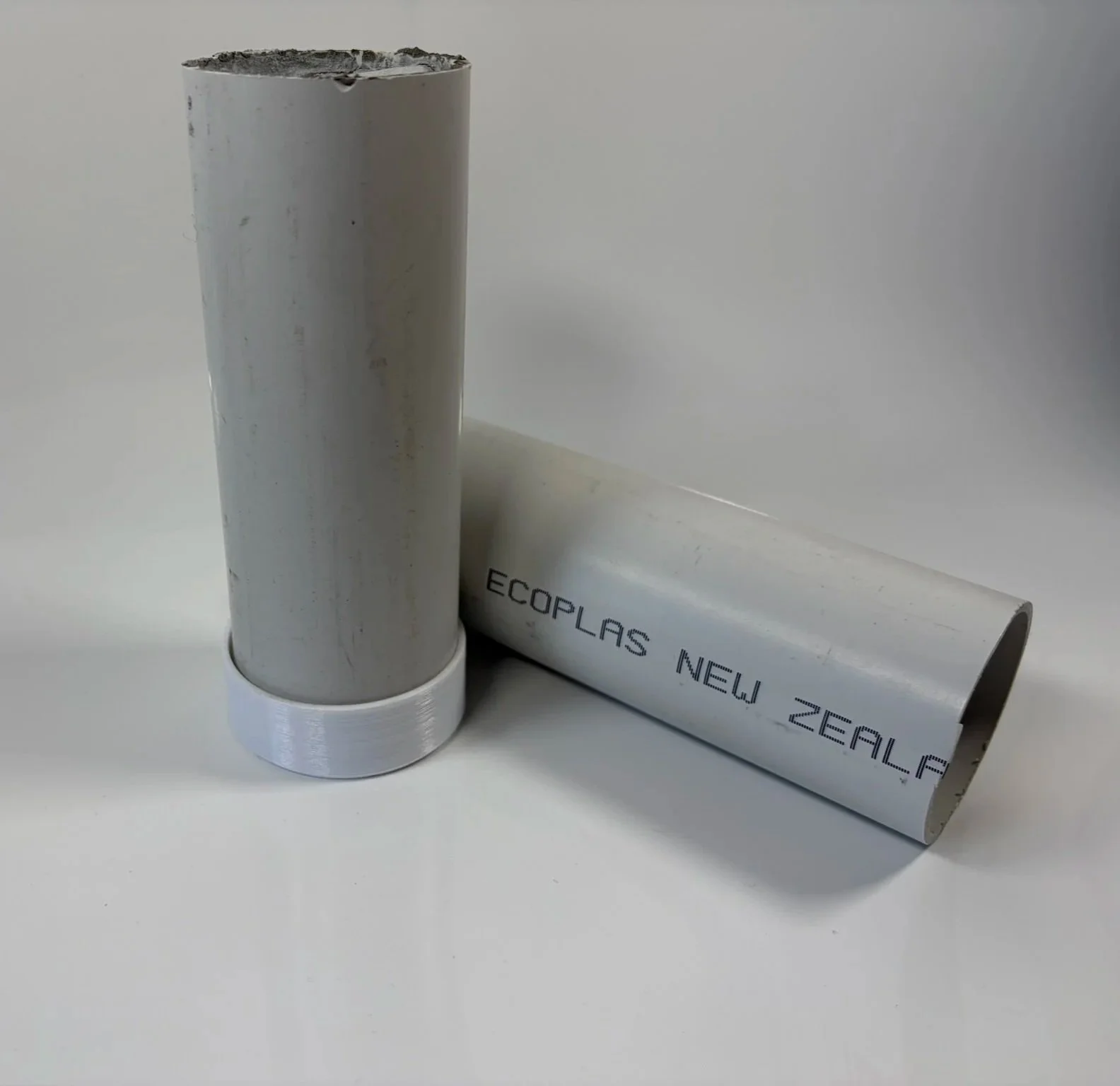 Two cylindrical aluminum tubes, one standing upright and the other lying down, with text 'ECOPLAS NEW ZEALAND' printed on the side of the lying tube.