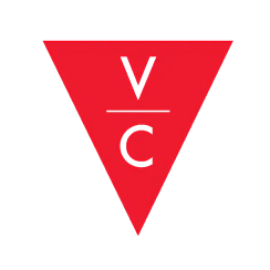 A red downward-pointing triangle with the letters V, C, and an underscore in black, arranged vertically inside. Village Cycles New Zealand Nelson.