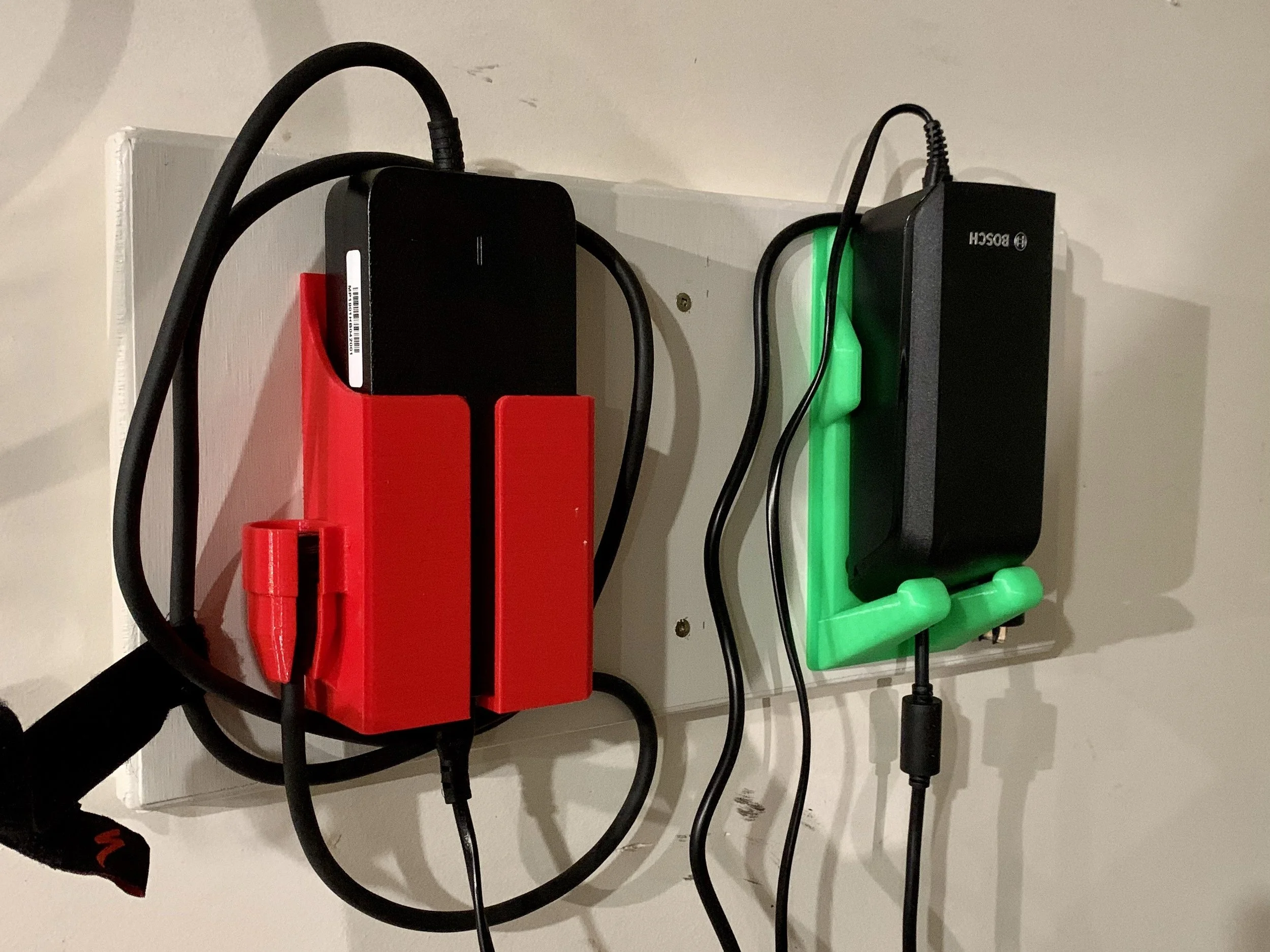 Electric E-Bike charging station with two chargers, one in red holder and one in green holder, mounted on a wall.